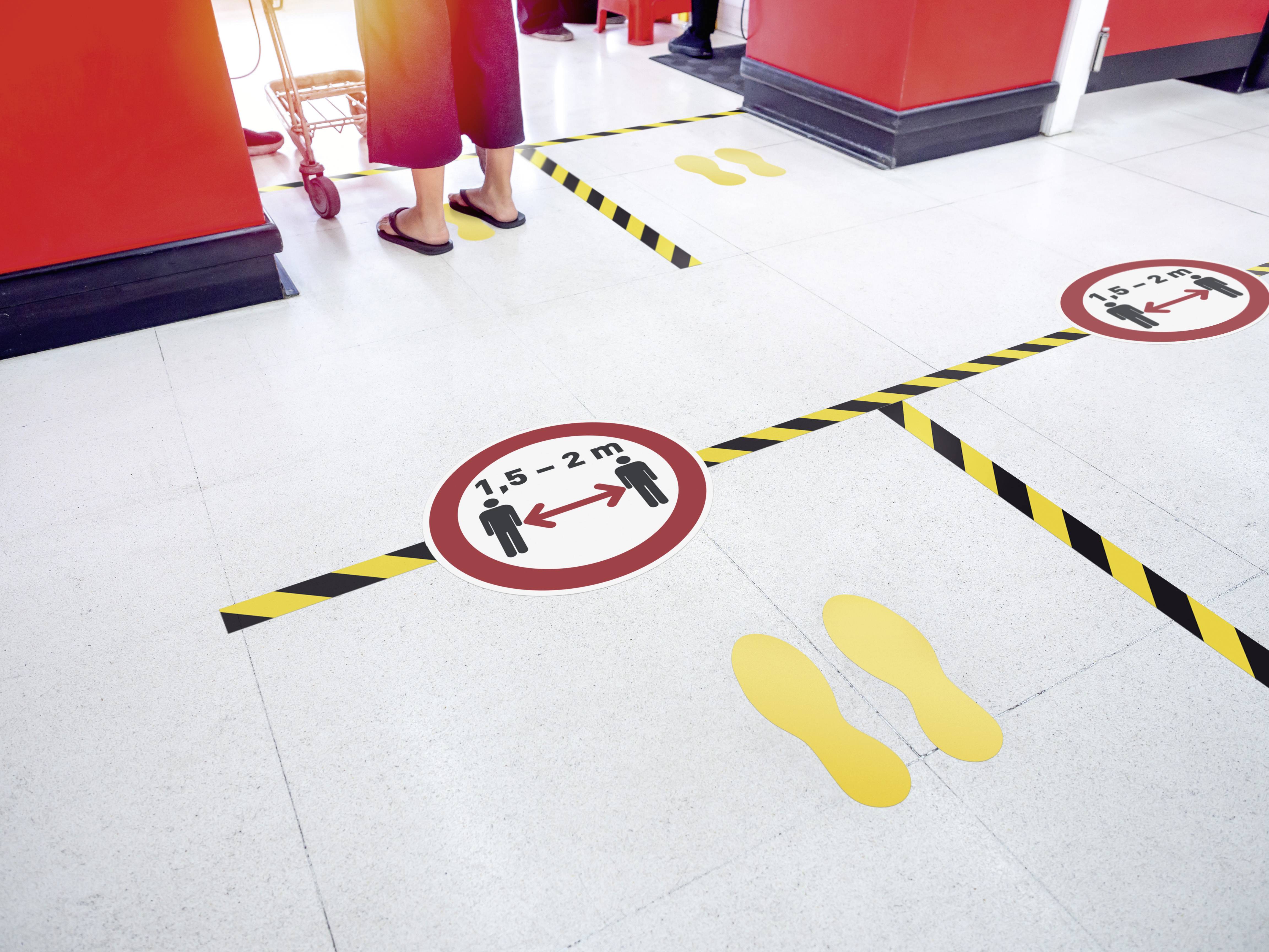 People in a shop are maintaining a social distancing of 1.5 to 2 metres. Yellow footprints and markings on the floor.