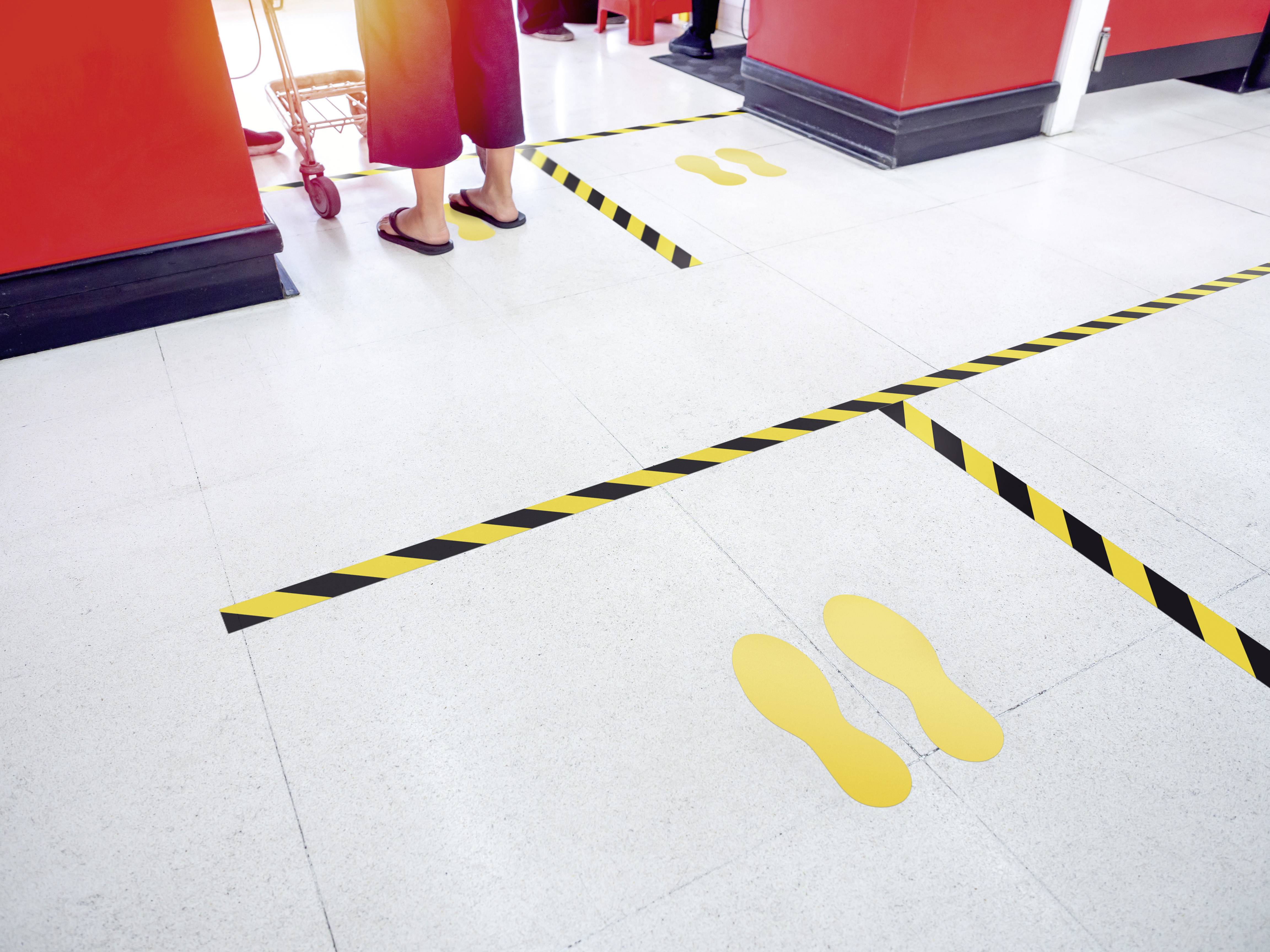 Yellow footprints mark the queuing area in a shop in front of the till, separated by yellow and black distancing markers.