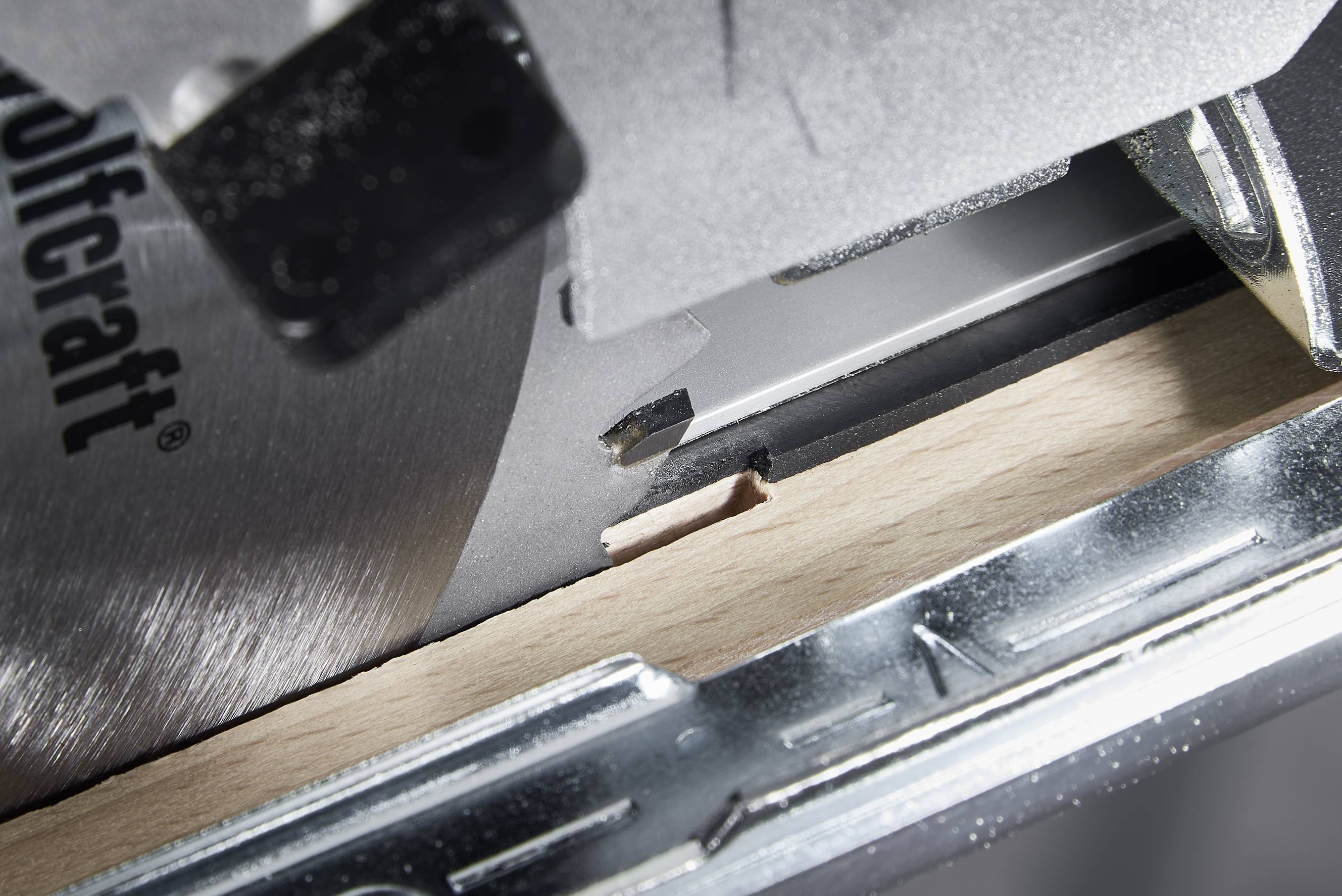 Close-up of a circular saw cutting through a wooden board. The metal frame of the saw is also visible.