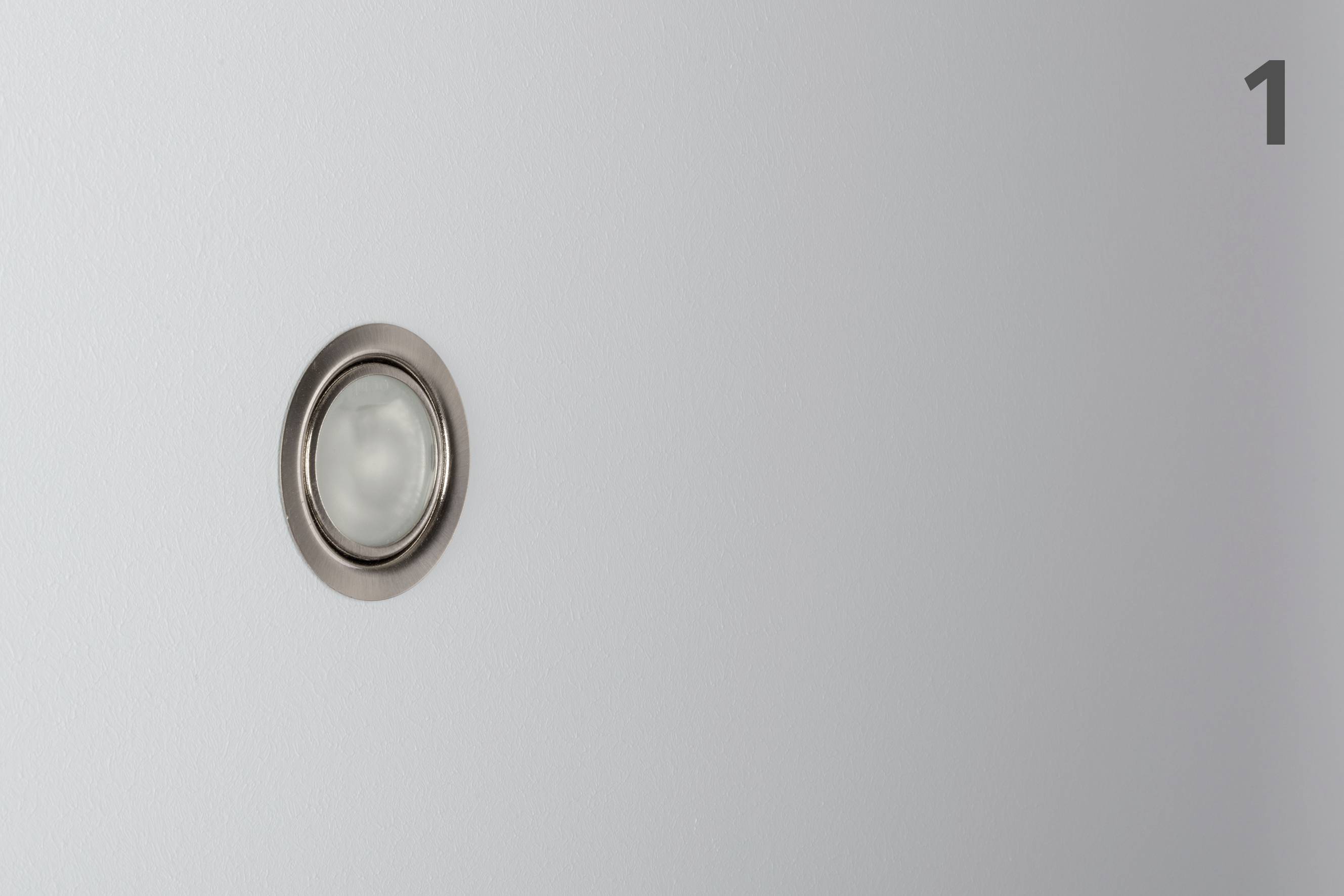 A single, round push button on a grey wall, marked with the number '1' in the top right corner.