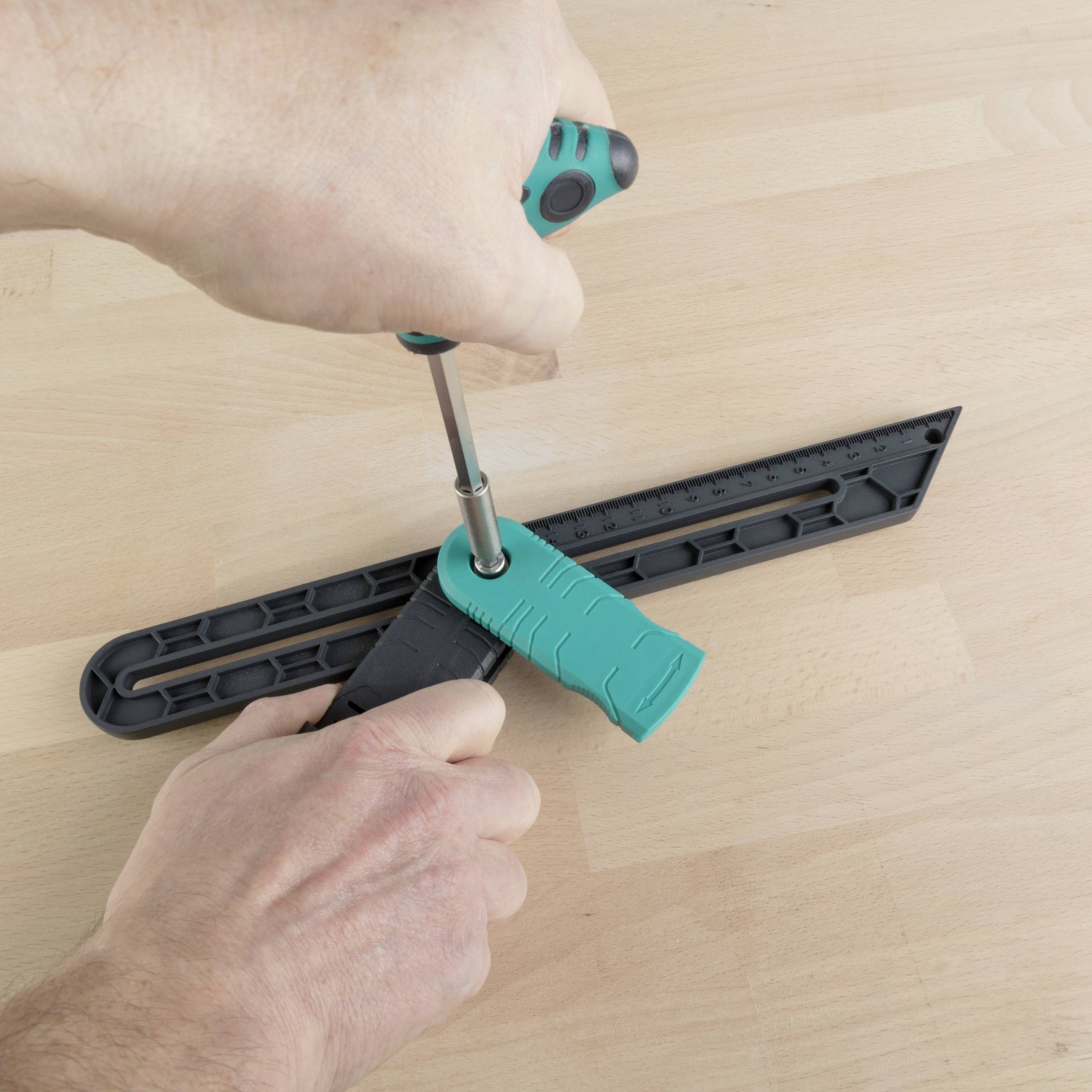 A person is adjusting a protractor by turning the handle. The protractor is resting on a wooden surface.