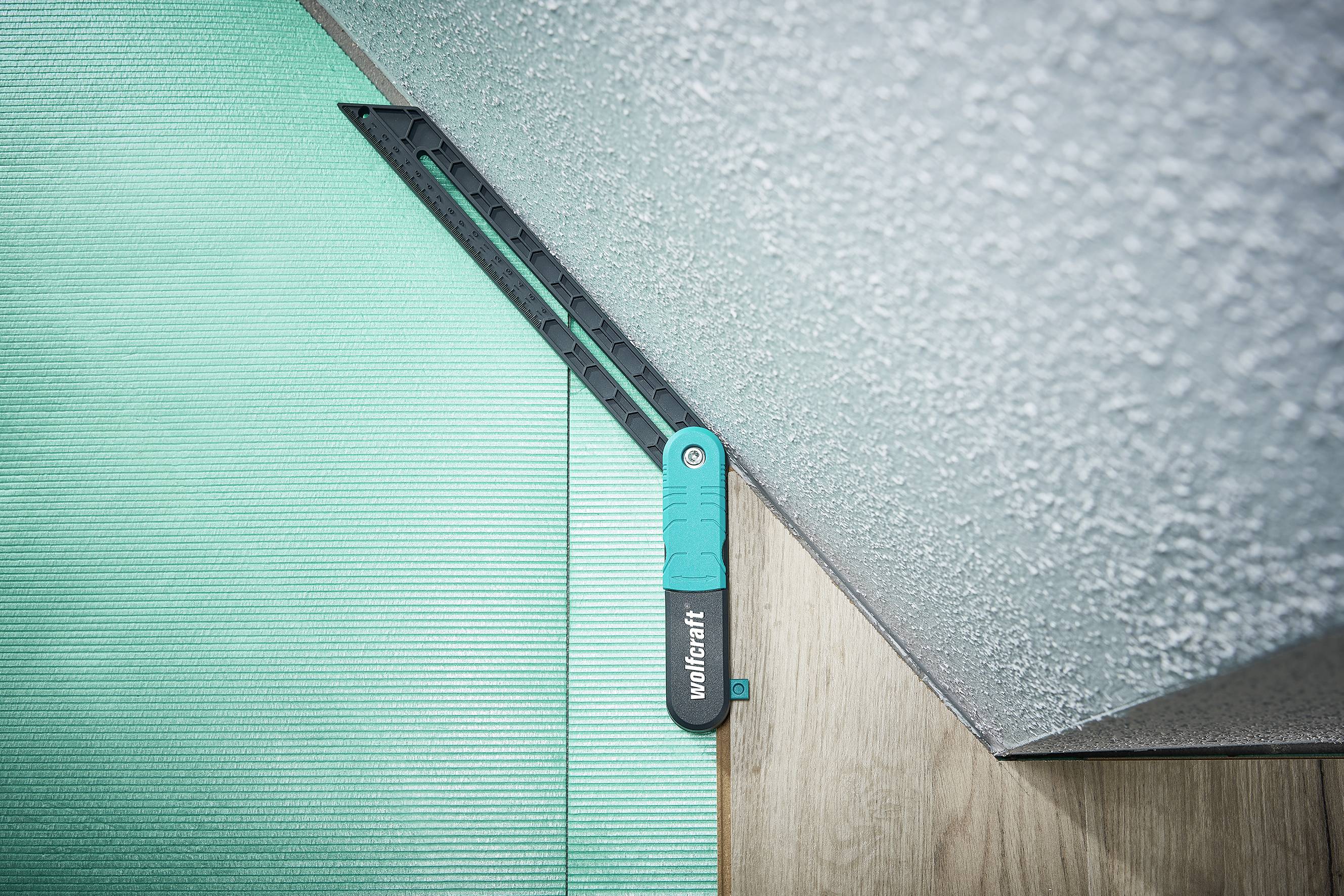 A protractor lies in a corner on a laminate floor and a green mat. It shows the angle between the wall and the floor.