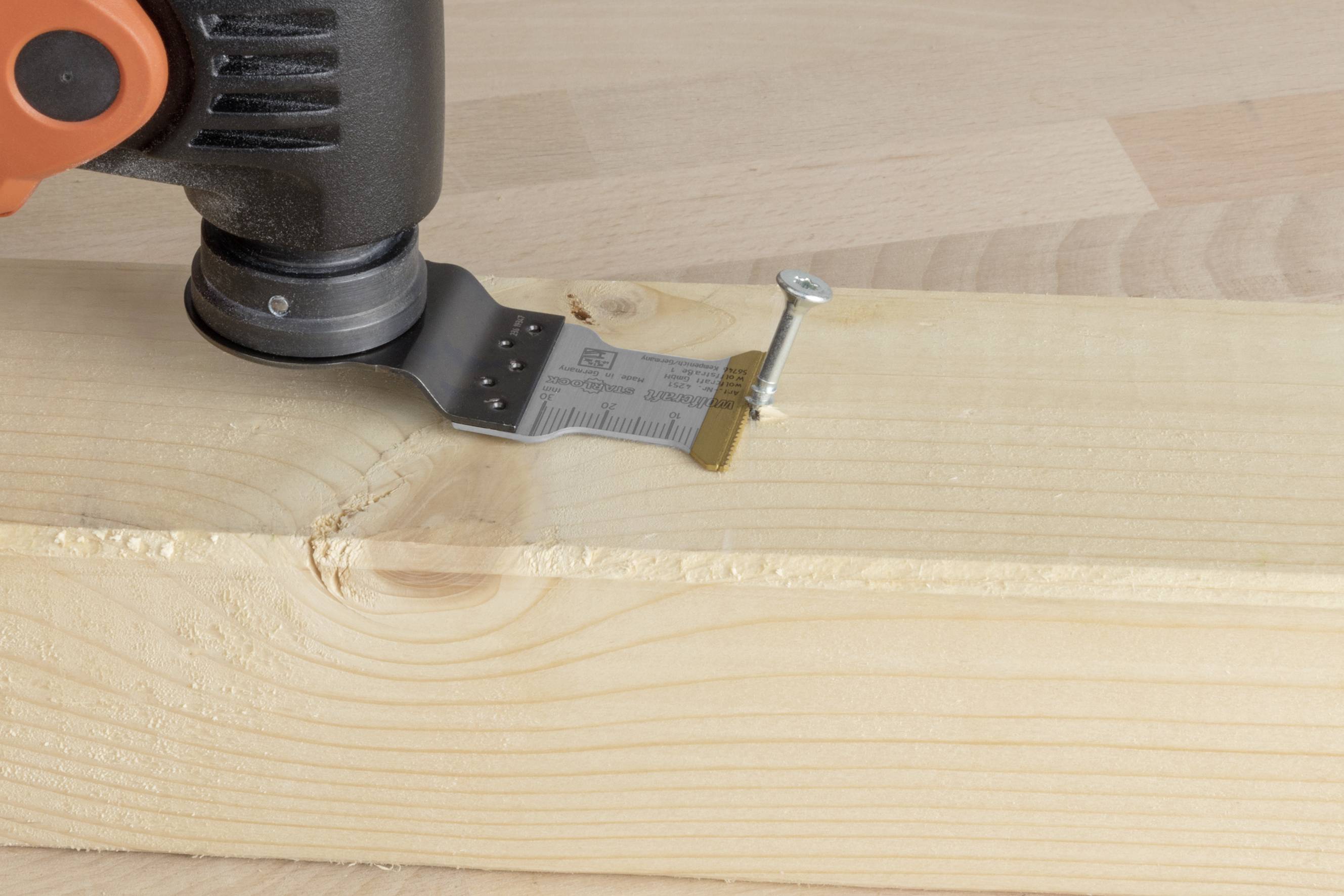 An oscillating saw cuts a nail fixed in wood. Worker's tool in action, focus on saw blade and nail.