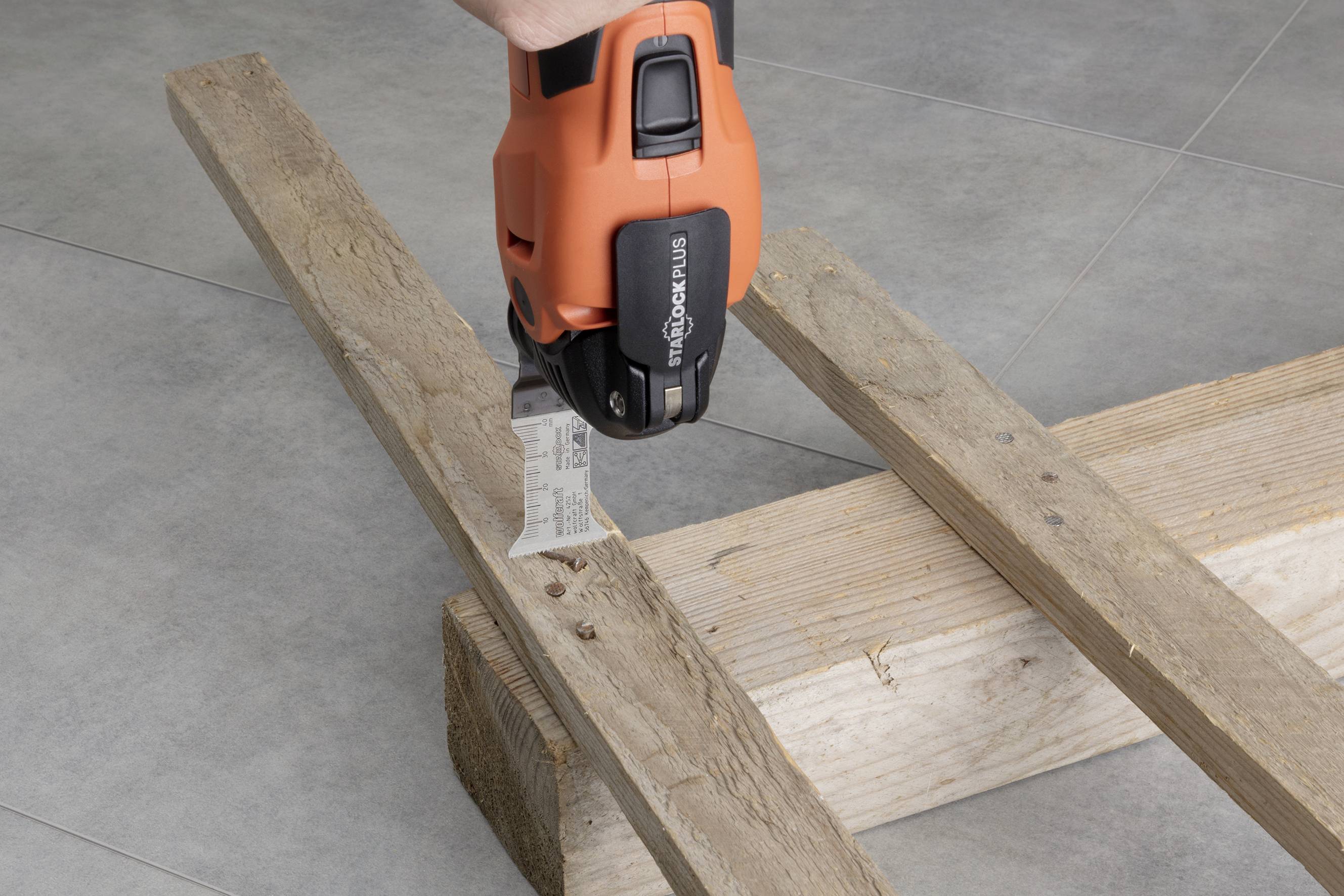 An orange electric saw cuts through a piece of wood resting on two other wooden planks.