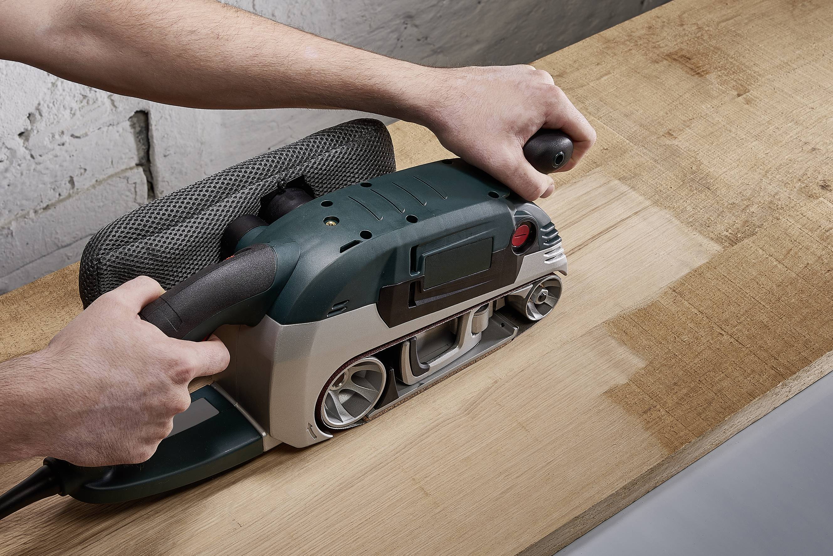 'A person is sanding a wooden board with an electric belt sander to smooth the surface.'