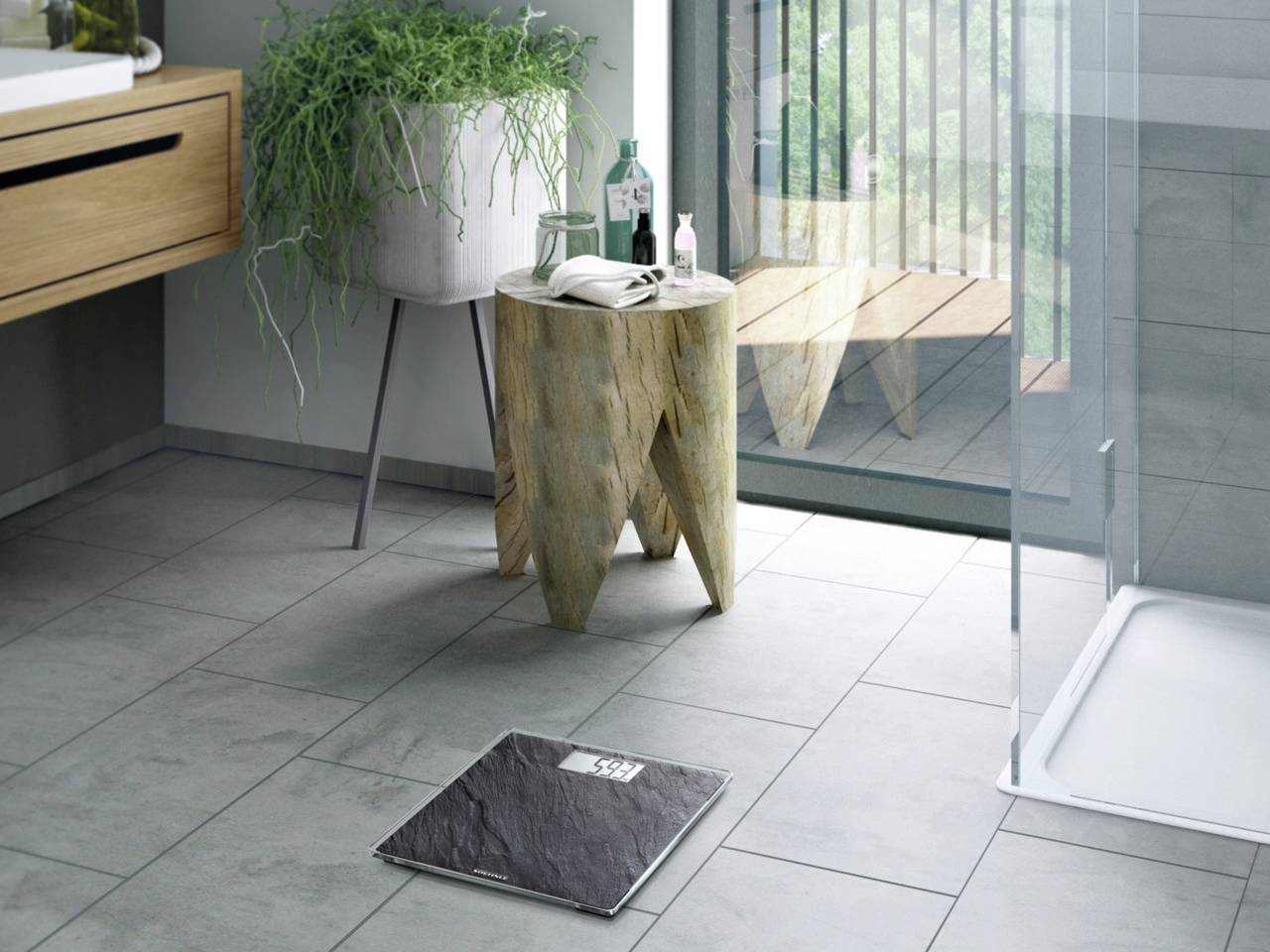 Modern bathroom with a glass shower, a wooden side table with plants and a black bath mat on grey tiles.