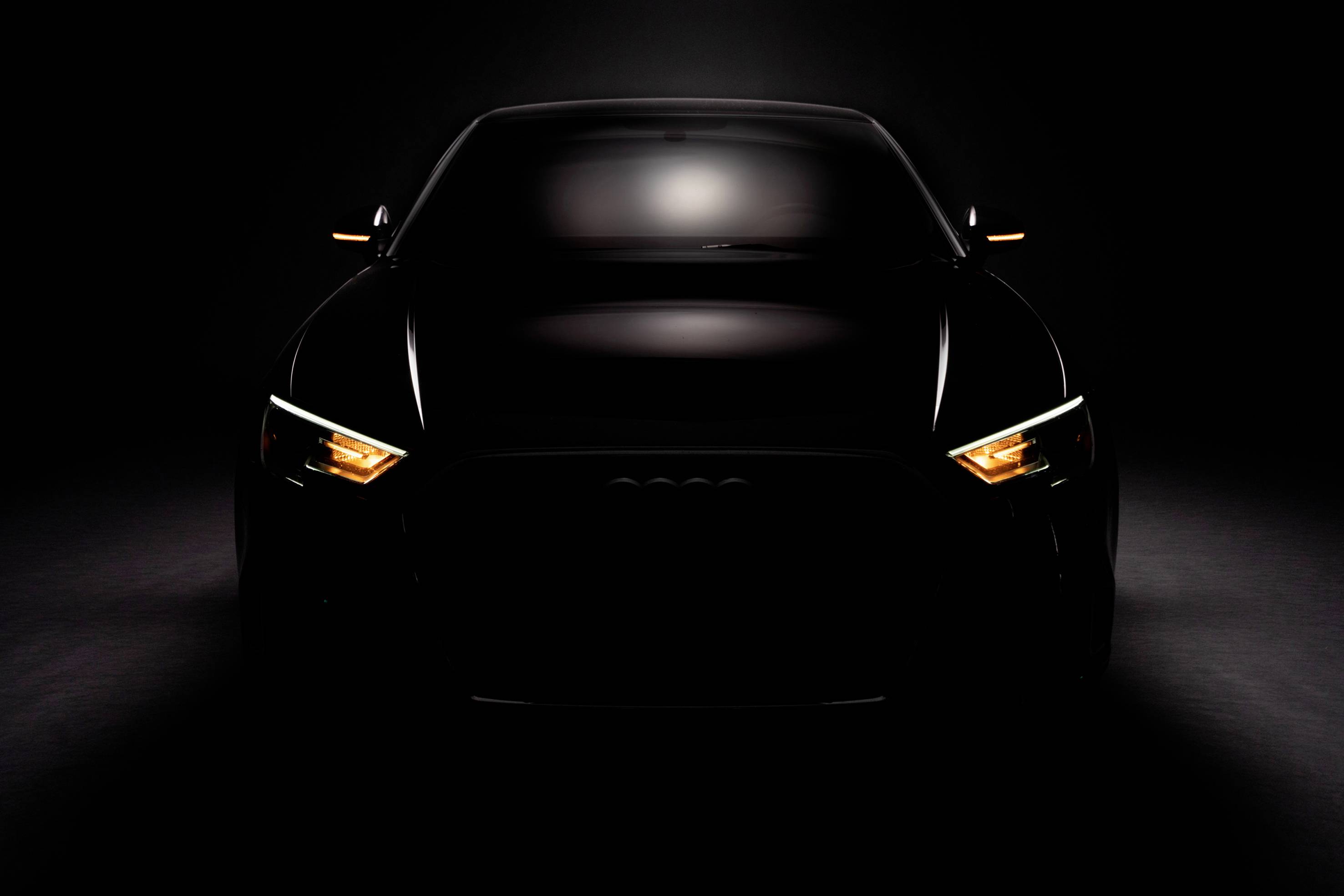 A black car in the darkness, with only the headlights illuminating, creating a dramatic and mysterious atmosphere.