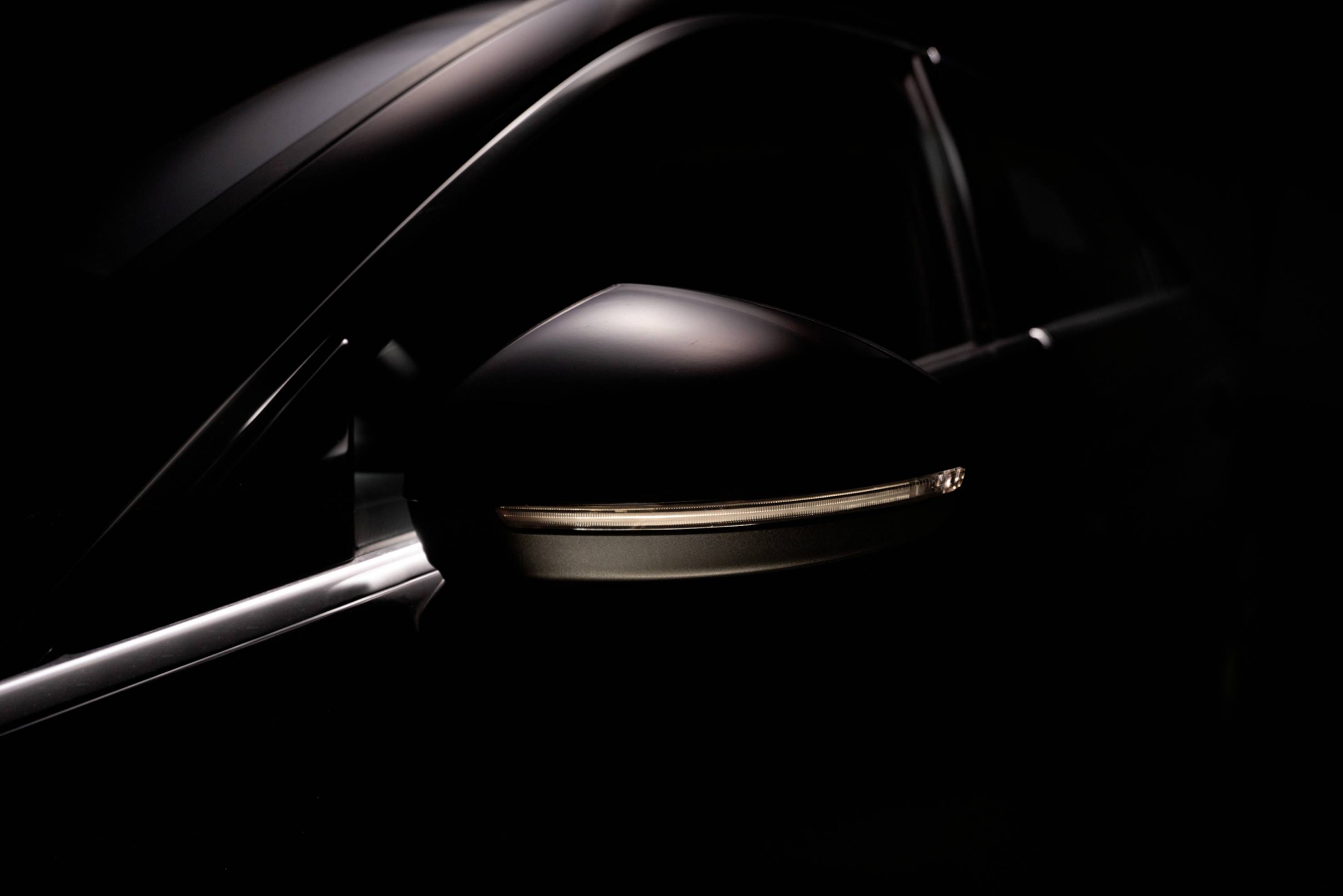 Black car wing mirror with integrated LED indicator light, viewed from the side, against a dark background.