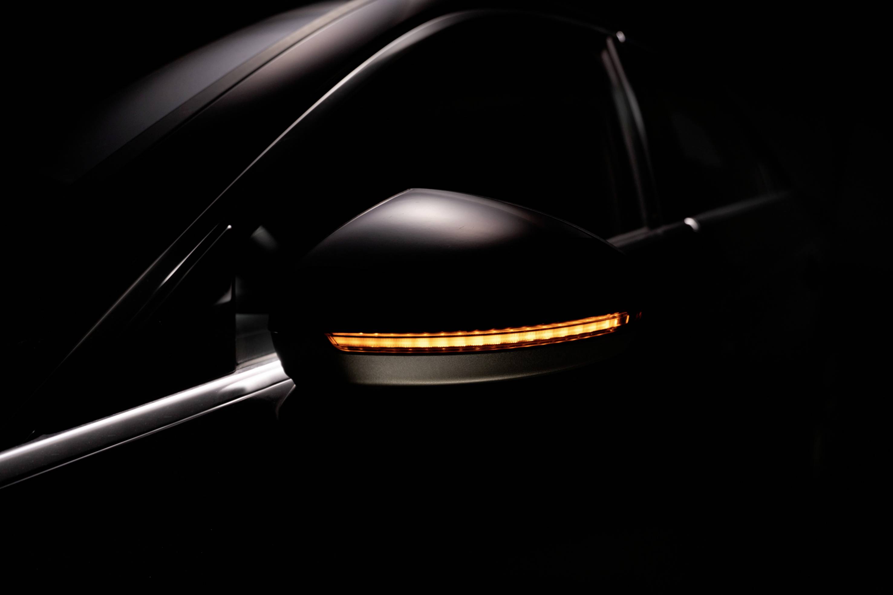A dark car with an illuminated yellow indicator light on its wing mirror, isolated on a black background.