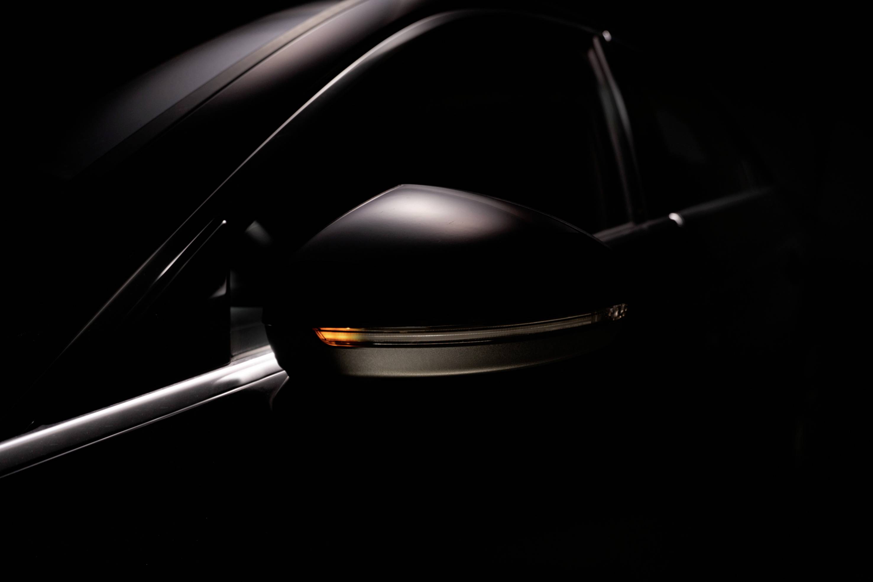 Close-up of a side car mirror in dim lighting, with an indicator light emitting an orange glow.