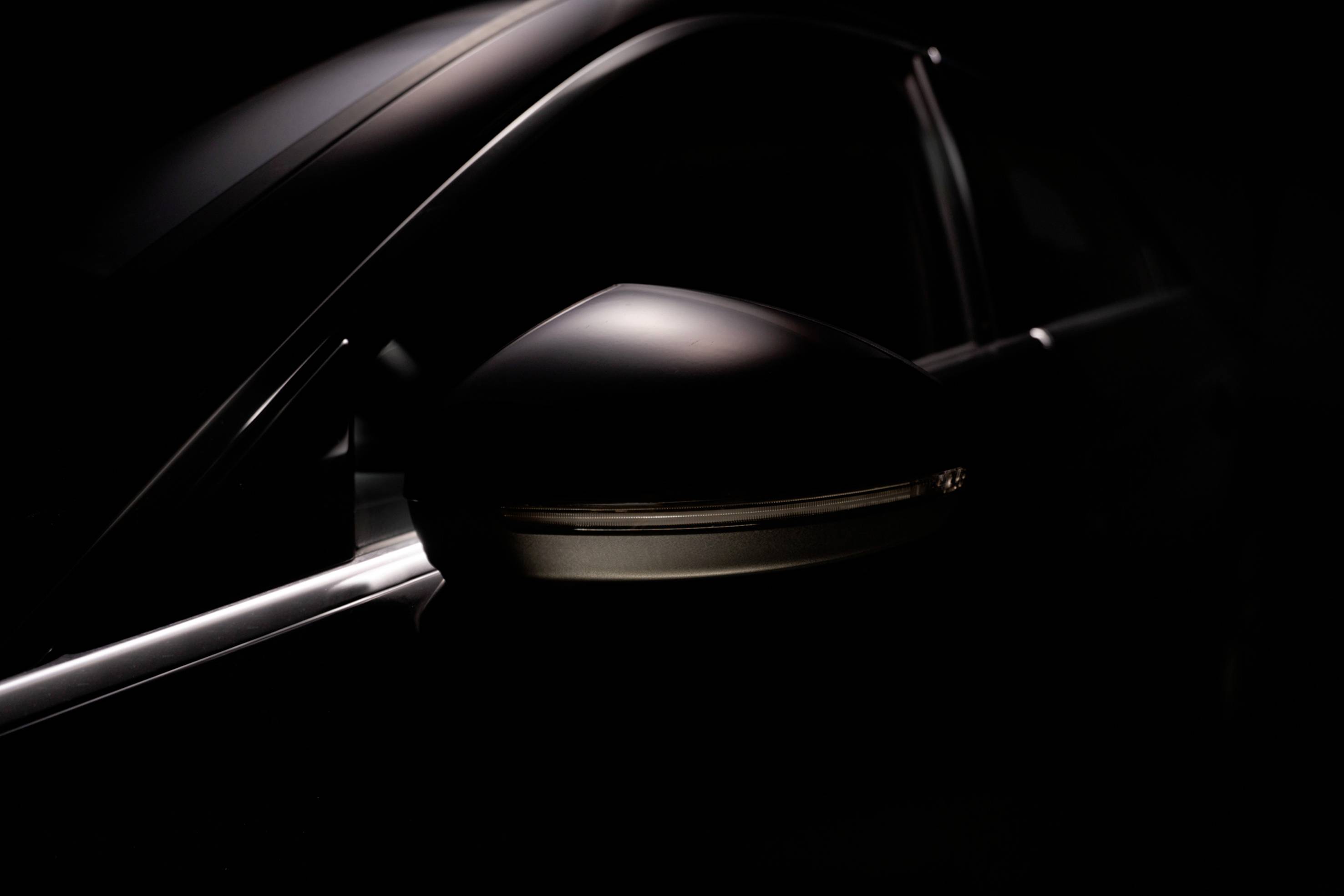 A dark, minimalist image of a car's wing mirror, emphasising its smooth surface and elegant shape.