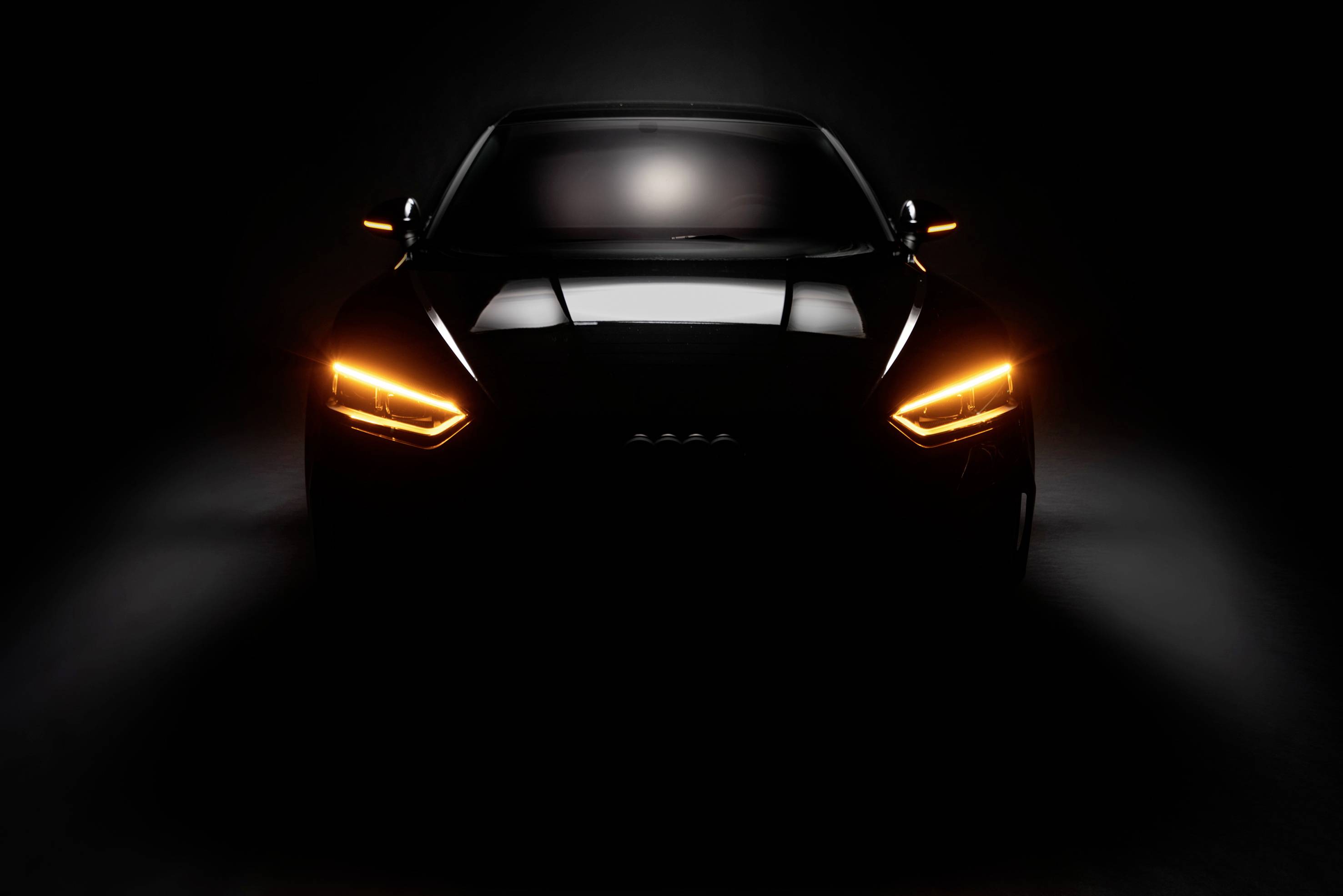 'Dark car with orange front light switched on, photographed head-on, stands out against a black background.'