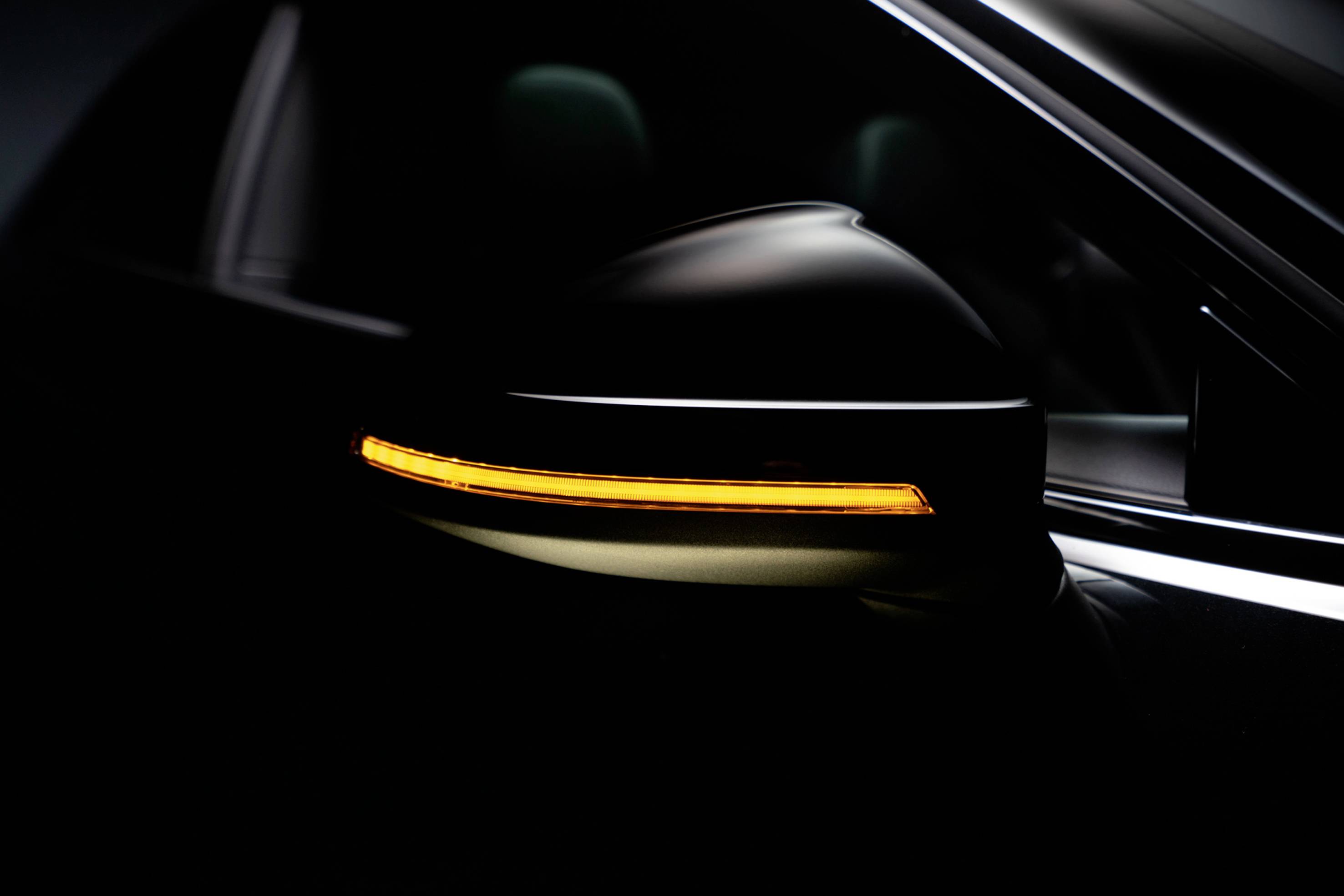 Close-up of a car wing mirror with an illuminated, glowing yellow indicator light in a dark environment.