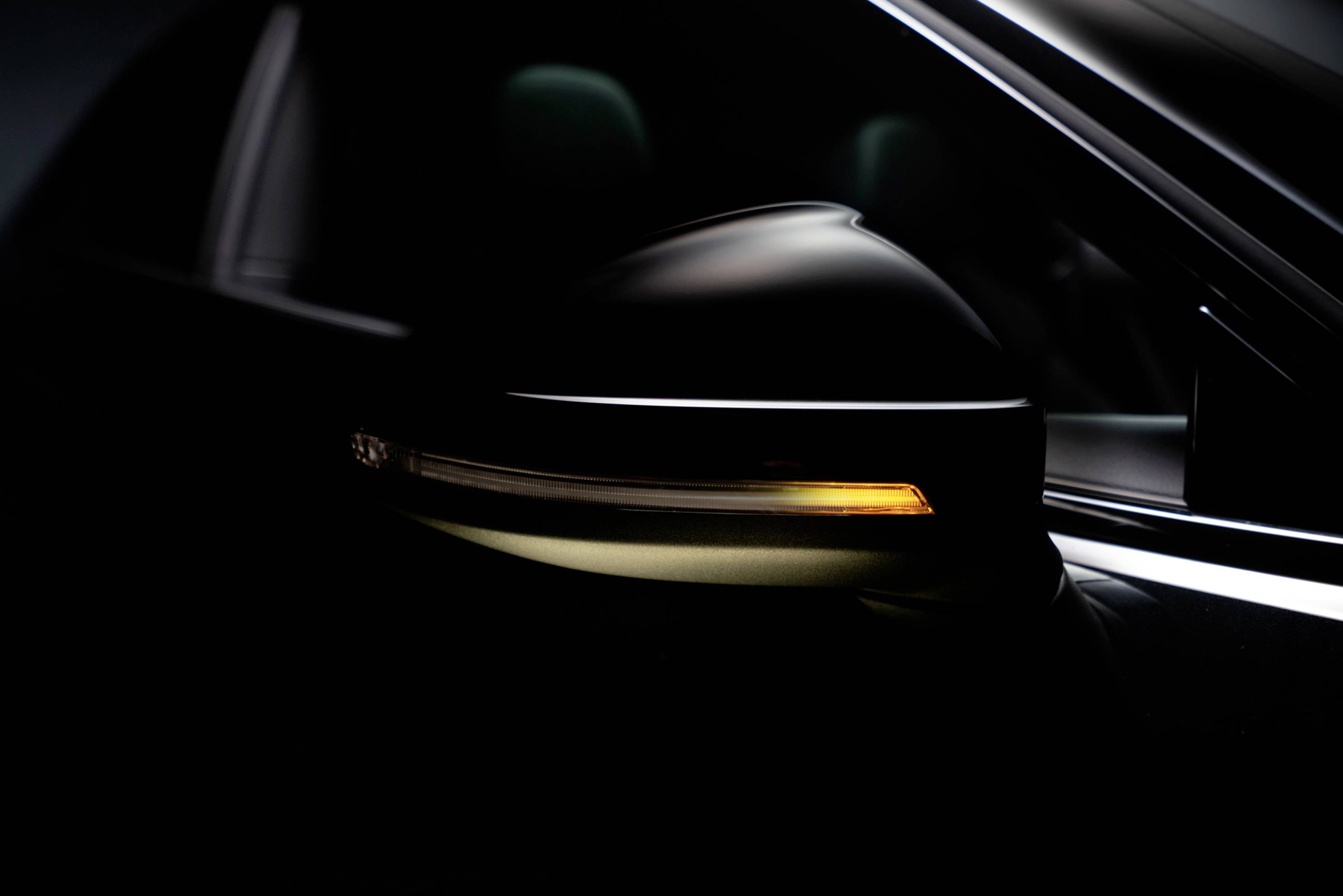 A side wing mirror of a car with a yellow indicator light switched on, glowing in the darkness.