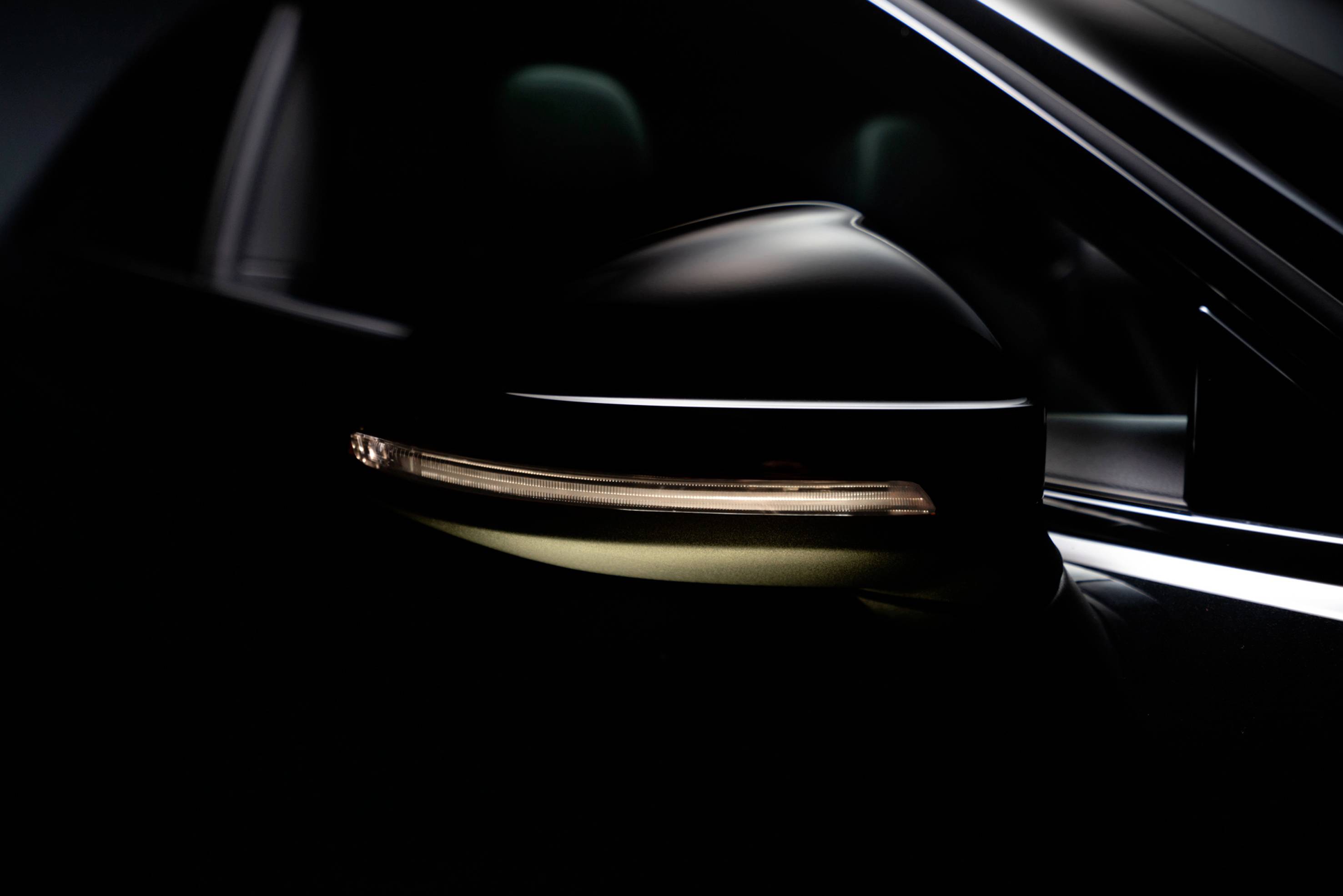 A dark car wing mirror with an integrated LED indicator light, gently illuminating in a dimly lit space.