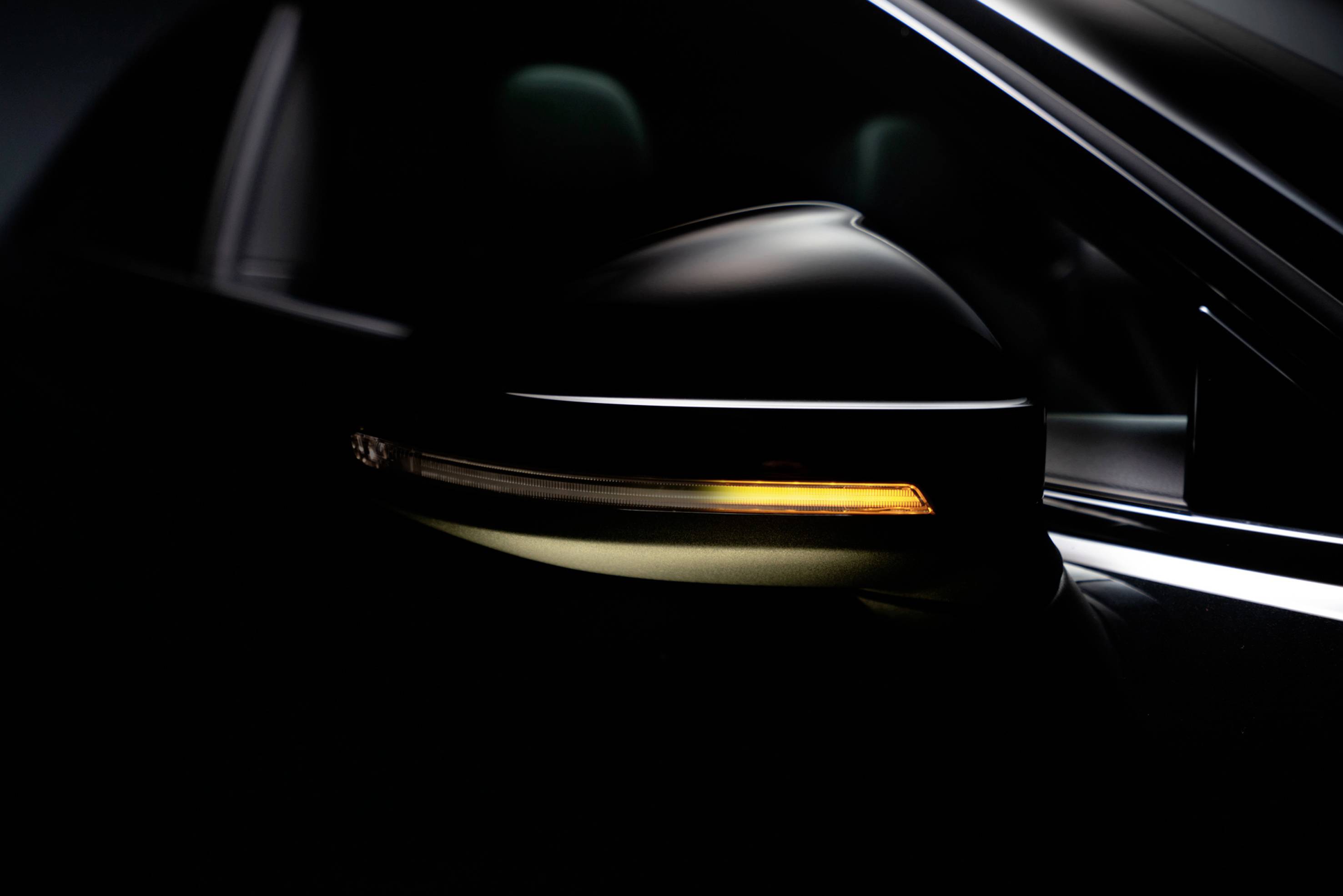 A close-up of a car's wing mirror with an indicator light that is illuminated, glowing a yellow-orange colour.