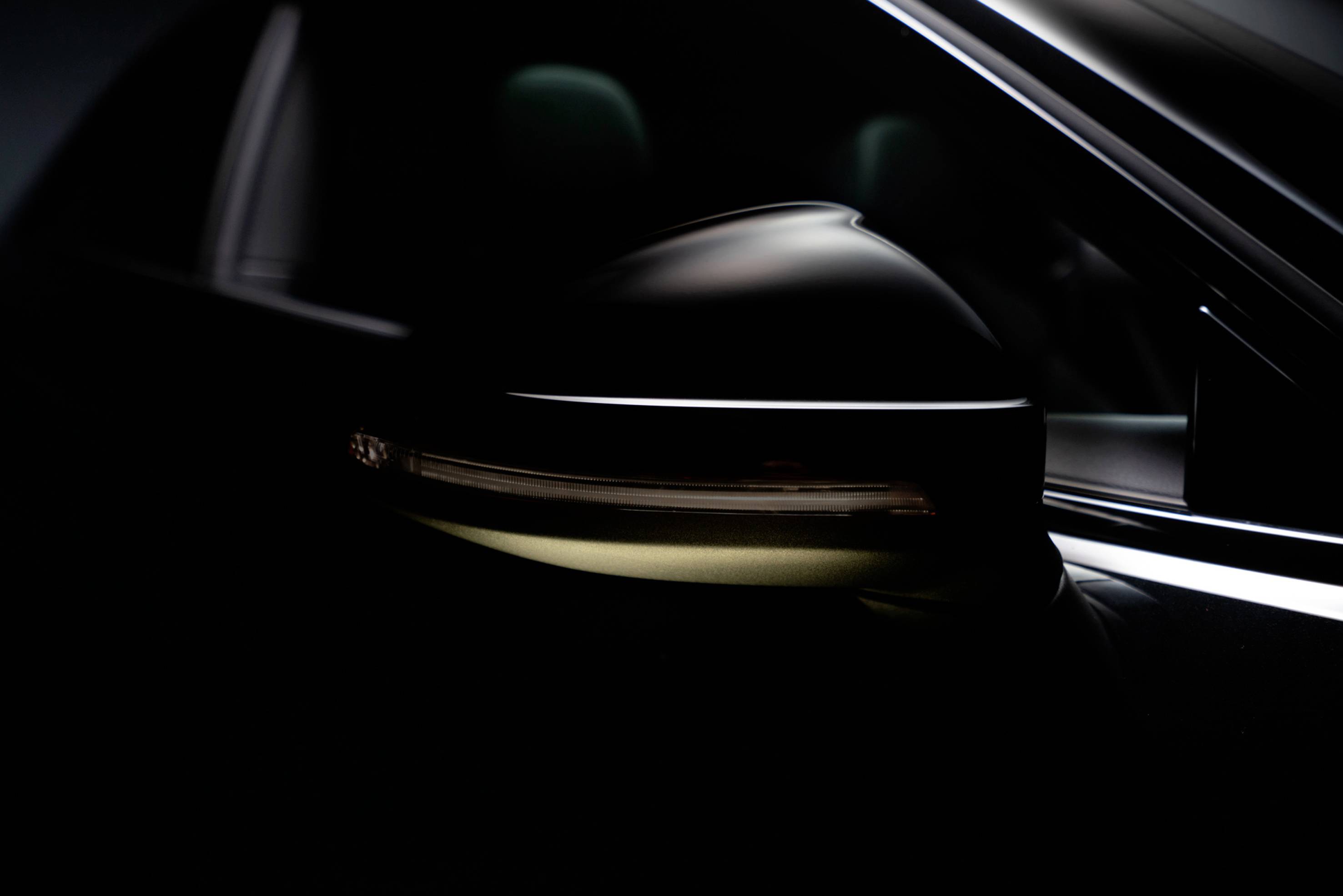 Close-up of a car's wing mirror in a dark environment, light streaks visible, focus on the elegant design.
