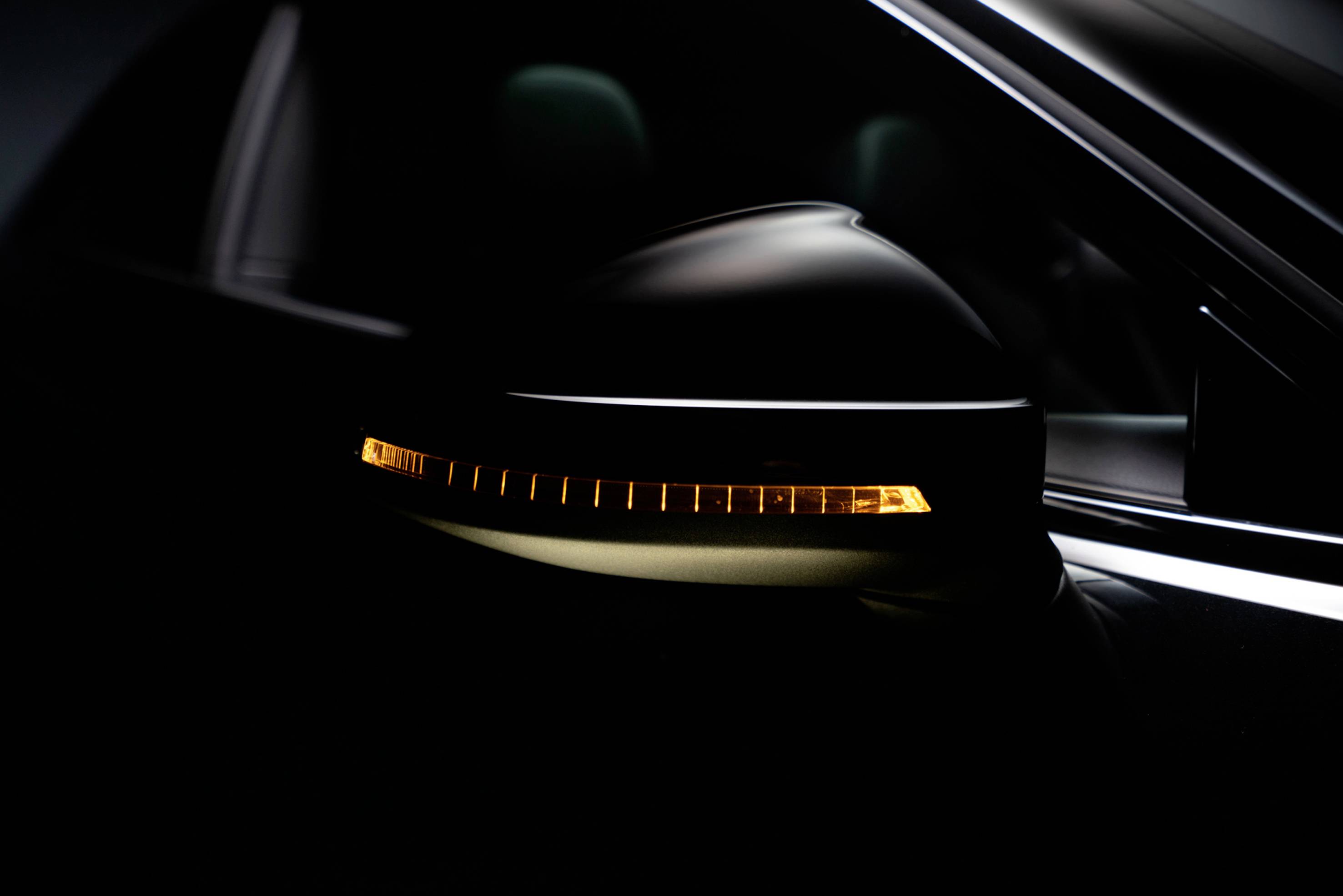 A dark wing mirror of a car with an illuminated yellow indicator light in an otherwise dark environment.