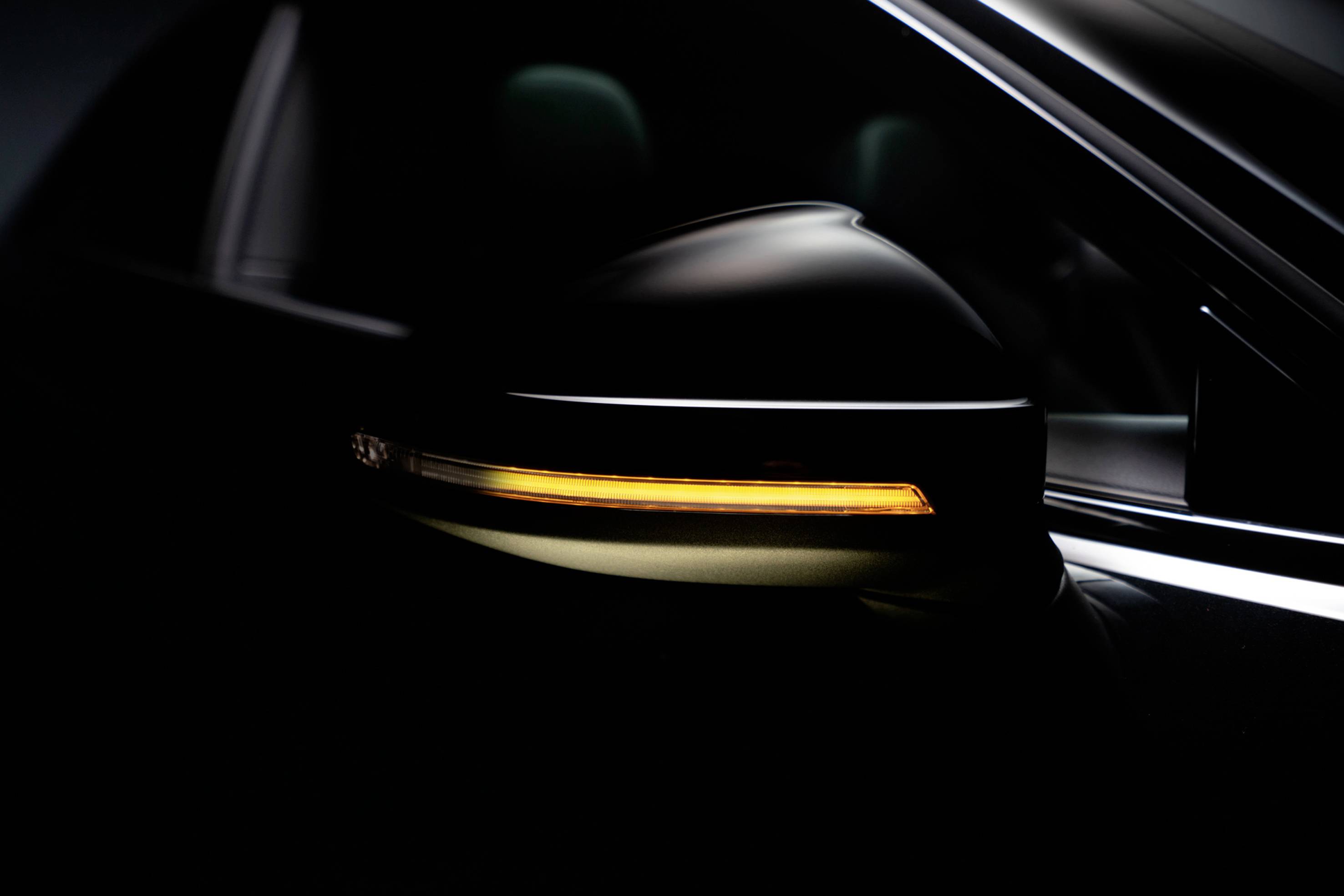 Close-up of a car wing mirror with an indicator light switched on, glowing orange against a dark background.