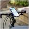 A smartphone displays a map app on a bicycle handlebar mount, showing directions. Hands are visible gripping the handlebars outdoors.