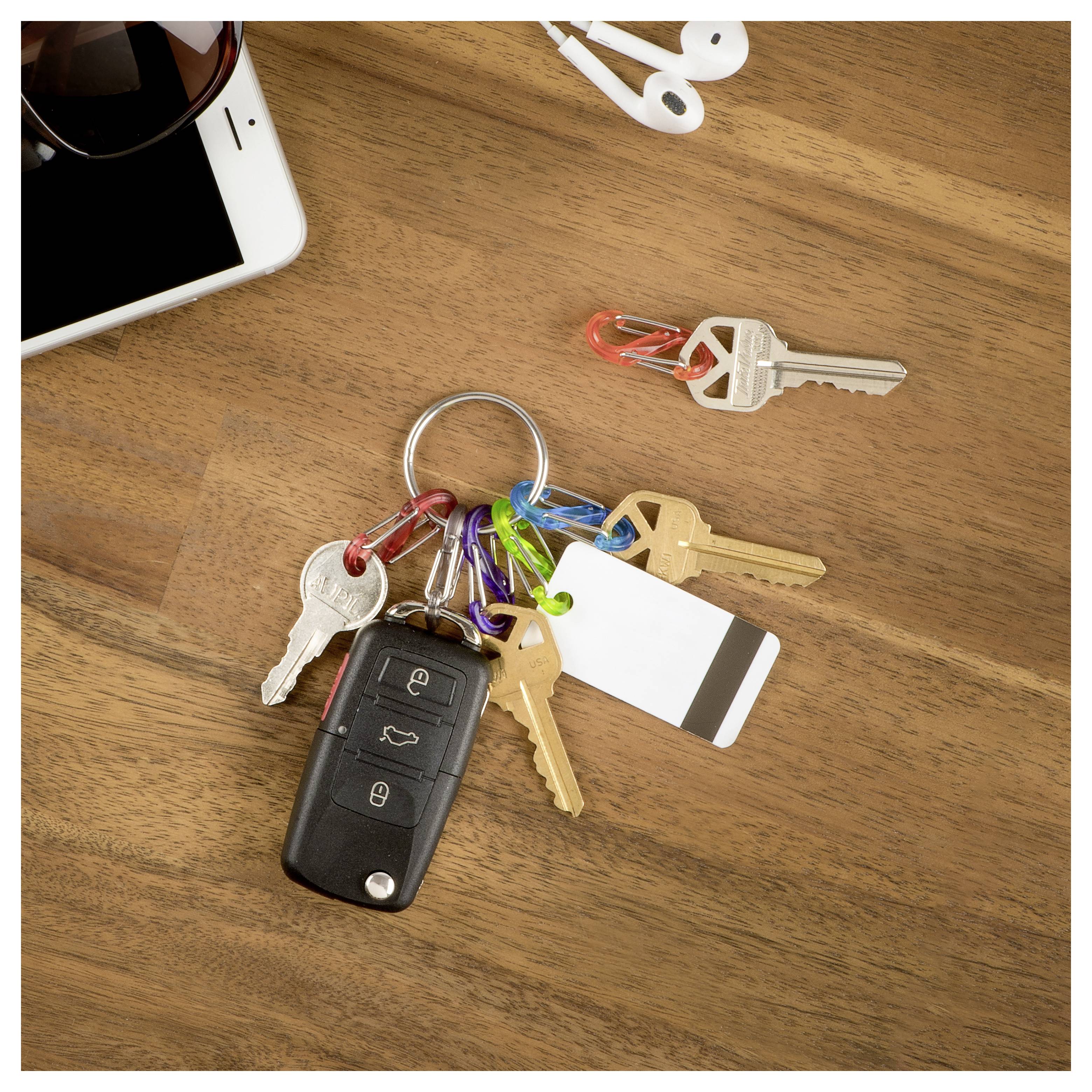 'A set of keys with a remote fob and colored keychains on a wooden table, next to a smartphone and earphones.'