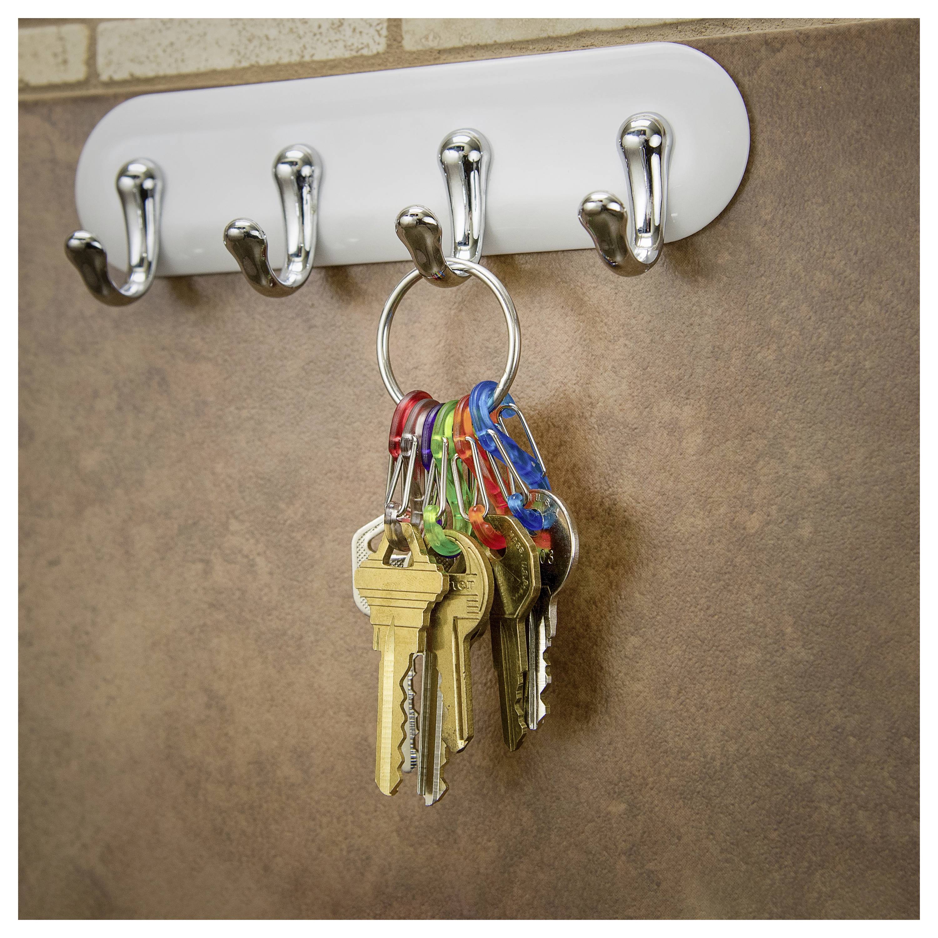 A ring of assorted keys hangs on a wall-mounted hook rack with five silver hooks against a brown tiled background.