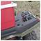 A red cooler secured with a bungee cord on the back of an ATV, parked on grass and gravel.