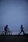 A person is jogging, another is cycling, both wearing reflective bands at dusk.