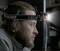 A man wearing a head torch in the darkness, looking intently. The lamp shines intensely forward, illuminating the area in front of him.