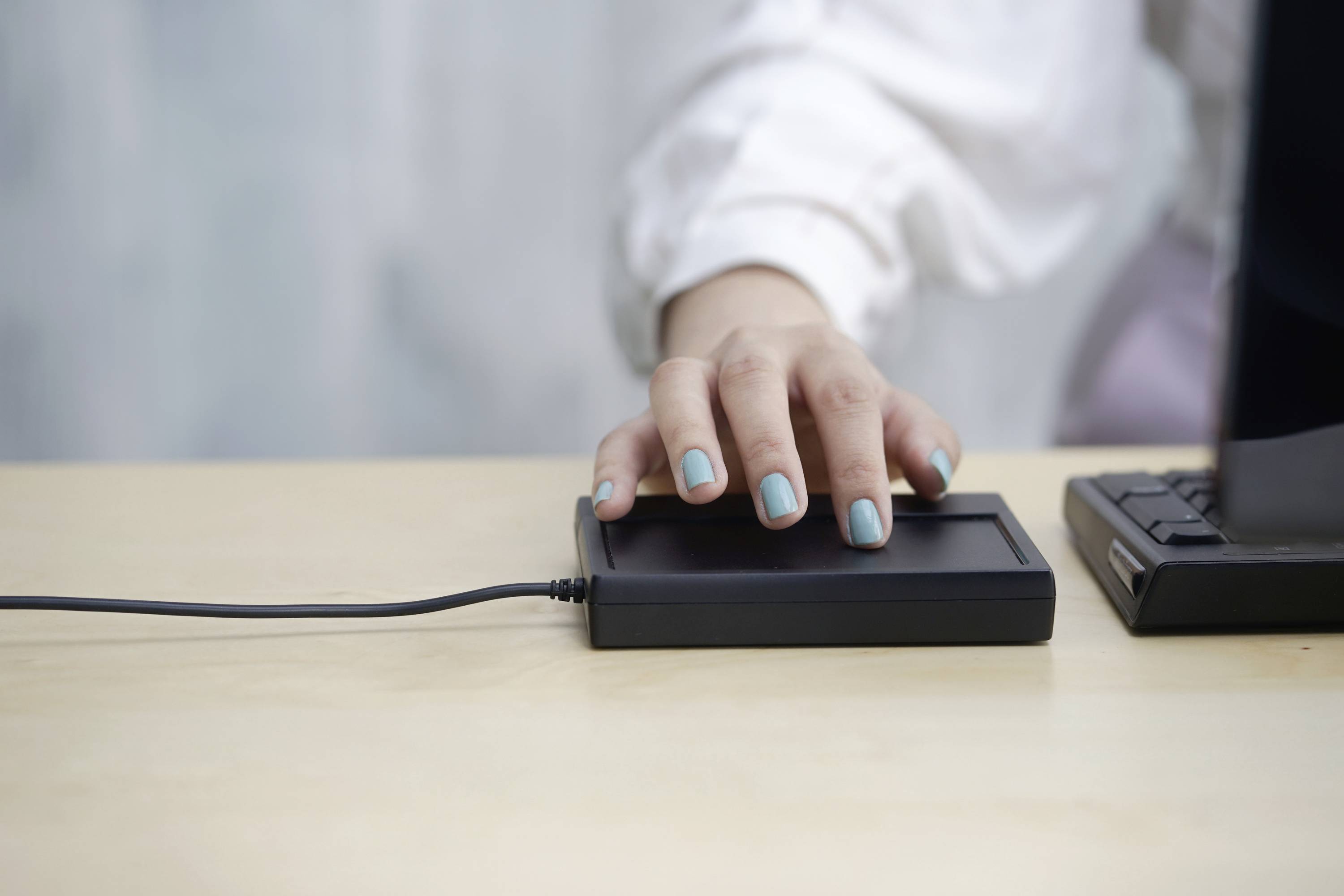 A hand with blue nails rests on an external hard drive, which is connected to a laptop via a cable.