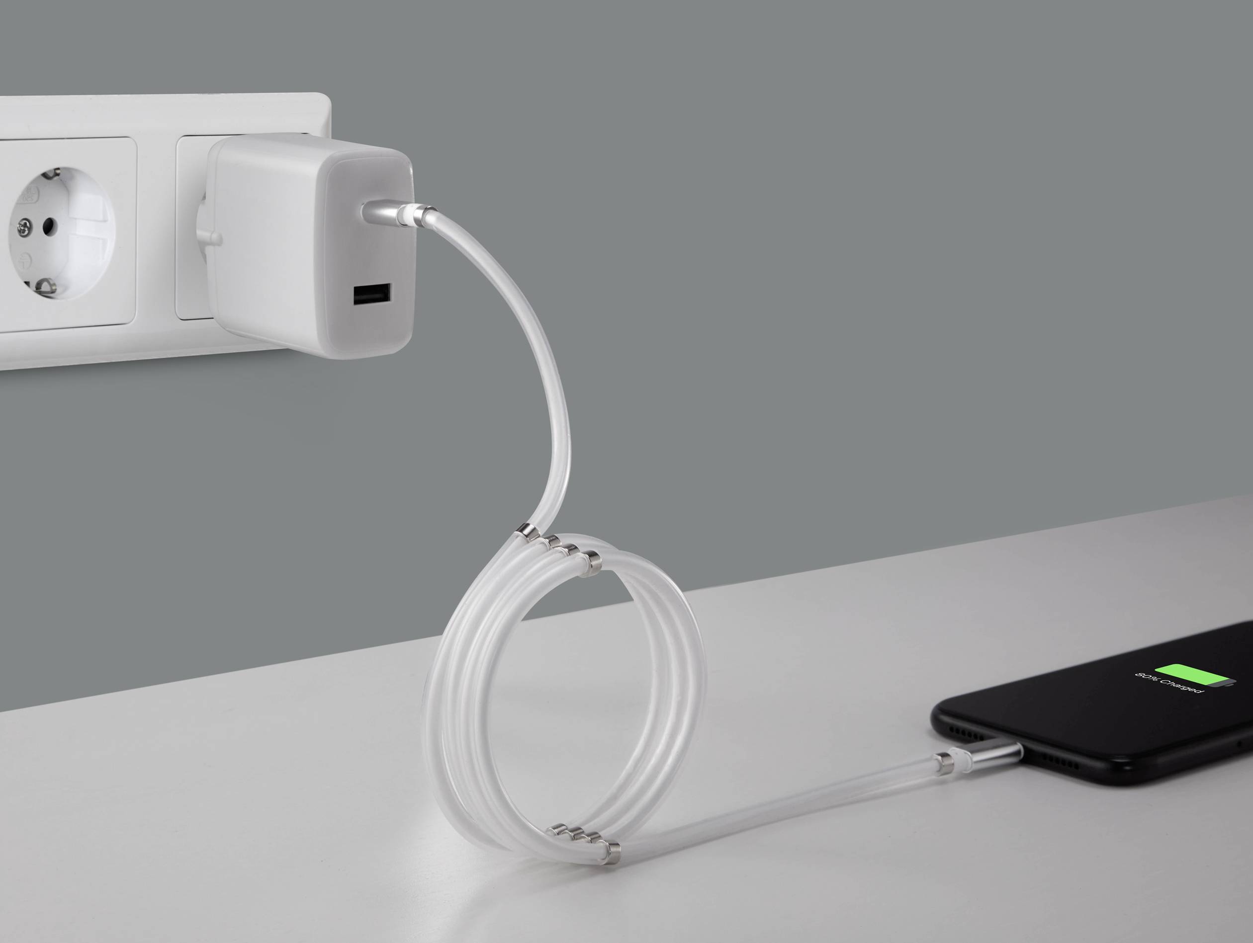 A smartphone is being charged via a USB cable from a charger plugged into a wall socket; the charging cable is creatively shaped like a spiral.
