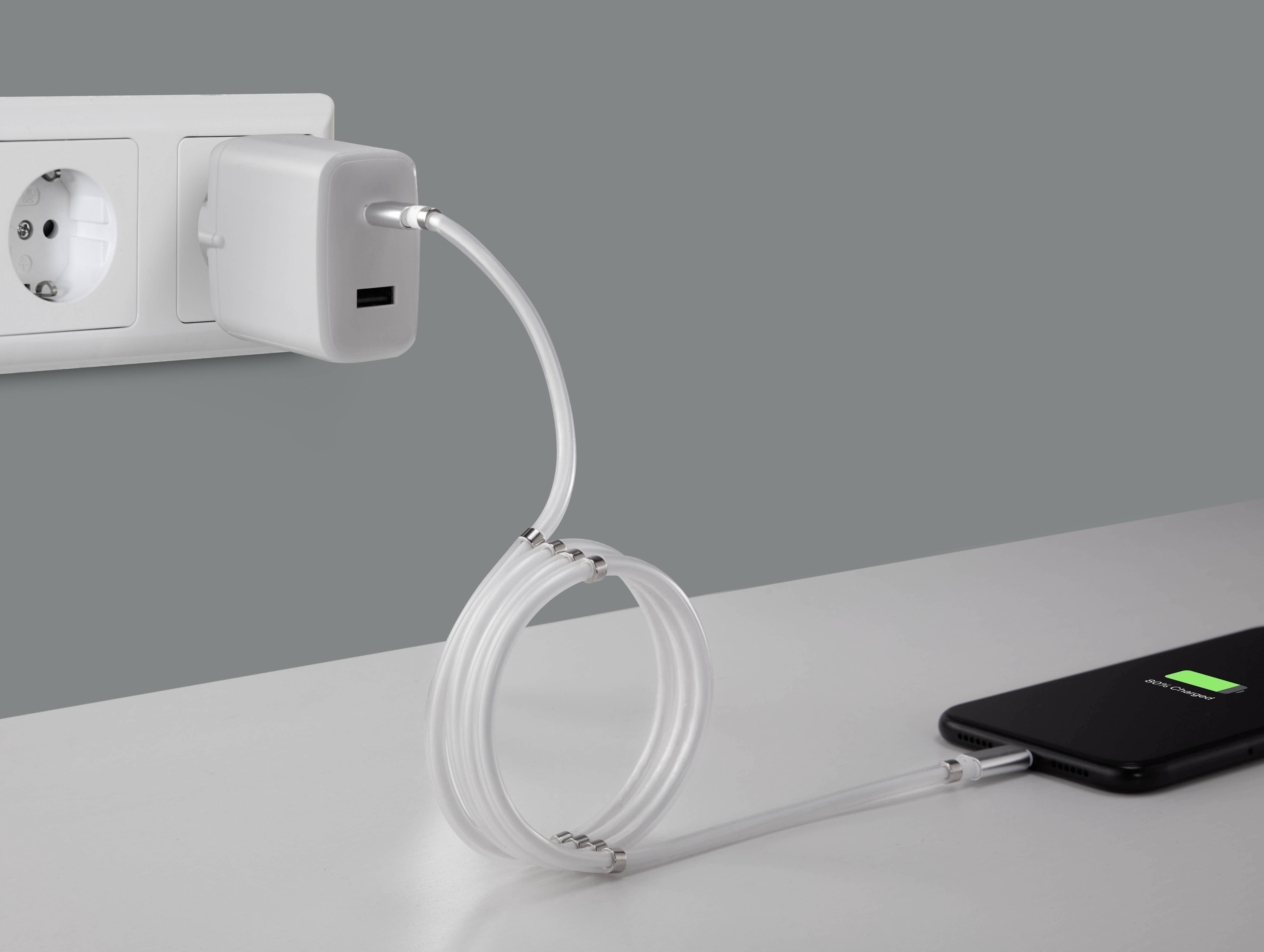 A smartphone on a table is charging with a spiral cable connected to a charger plugged into a wall socket.
