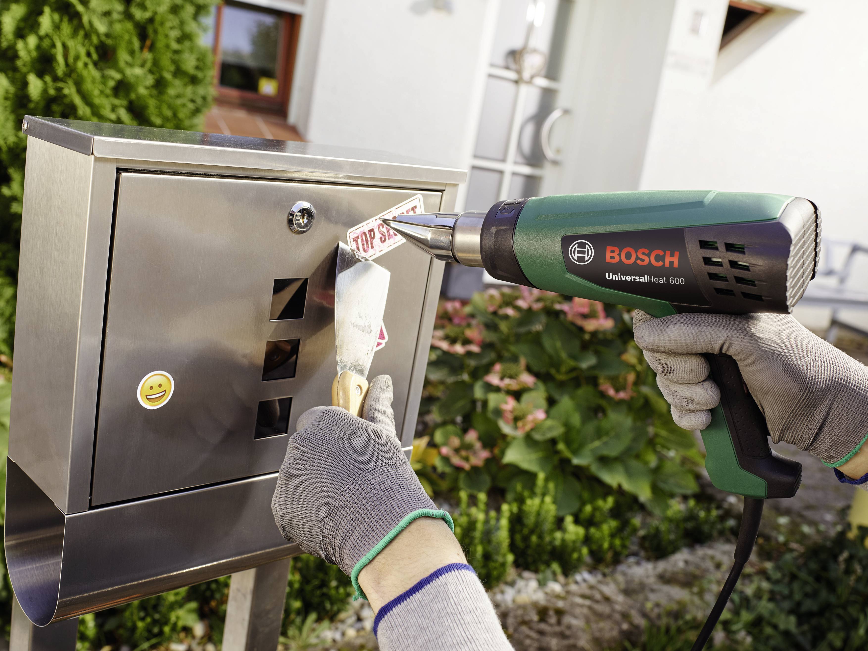 A person is removing a sticker from a metal letterbox using a hot air blower in order to clean or repair it.