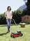 A person is mowing the lawn with a red lawnmower. In the background, there is a garden shed, plants, and trees.