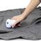 A hand is using an electric lint remover on a grey fabric to remove lint and fluff.