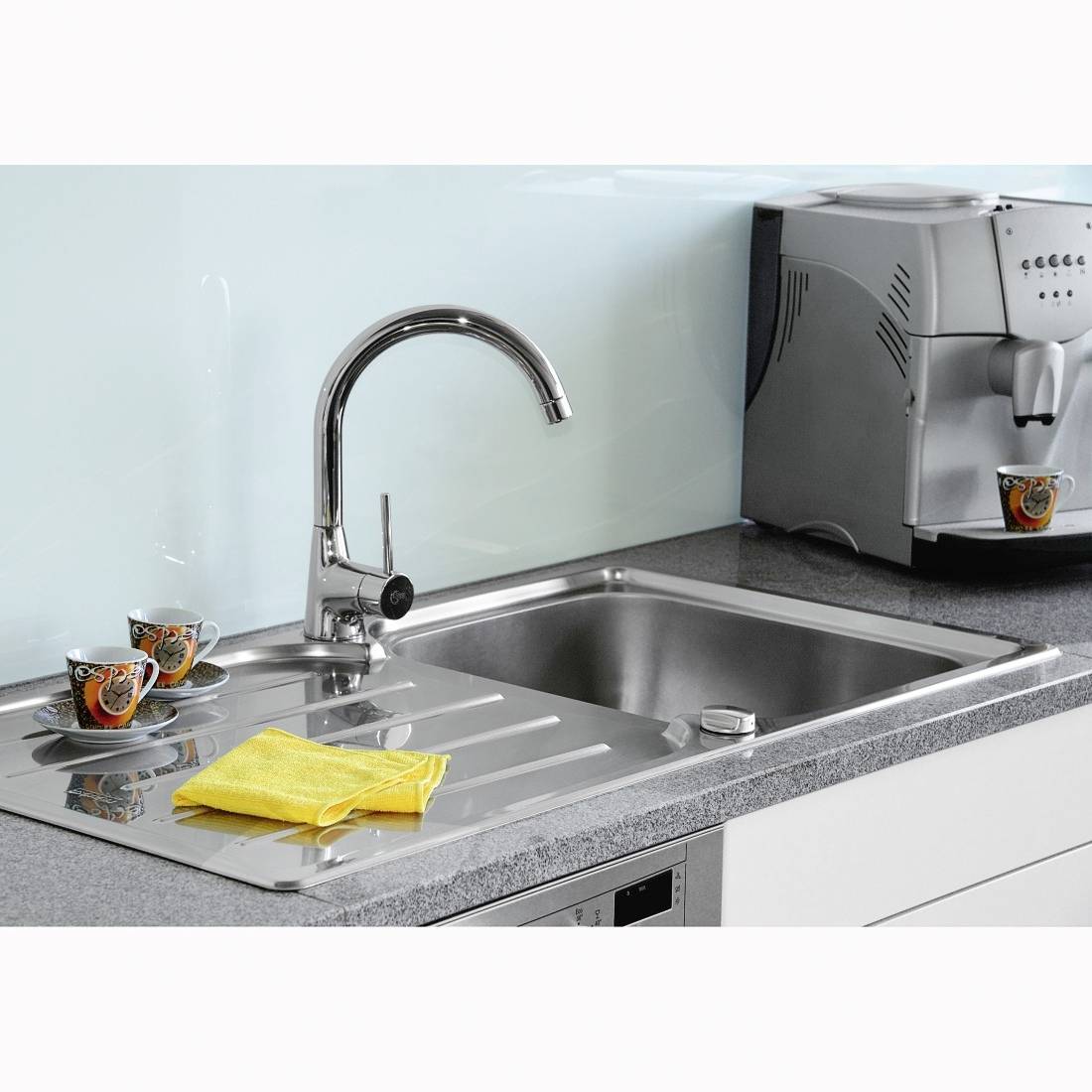 Kitchen worktop with sink, tap, two coffee mugs and a yellow cleaning cloth. To the right stands a coffee machine with a cup.