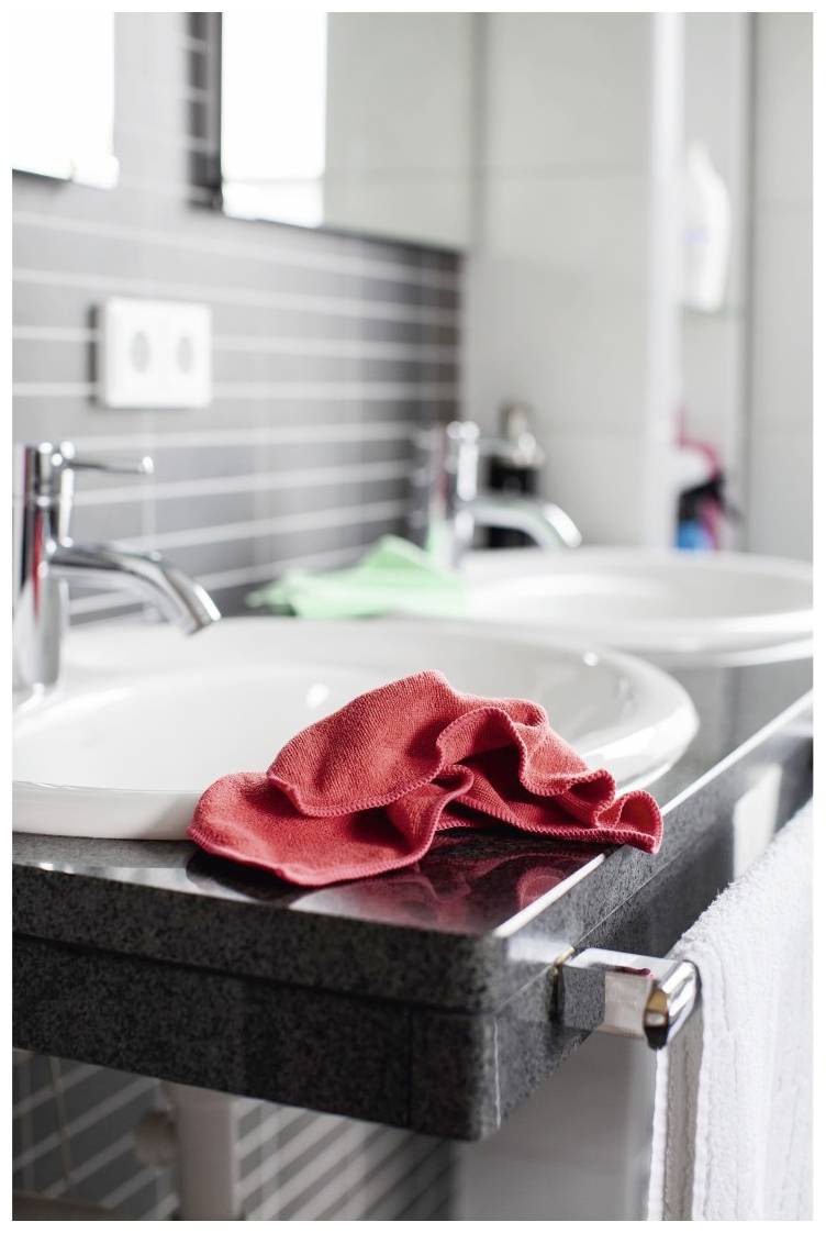 Two washbasins with modern taps, a red towel on the shelf and a white towel to the side.