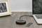 'A round adapter with a cable connects a laptop on a wooden table. A picture frame stands in the background, with a memory module lying beside it.'