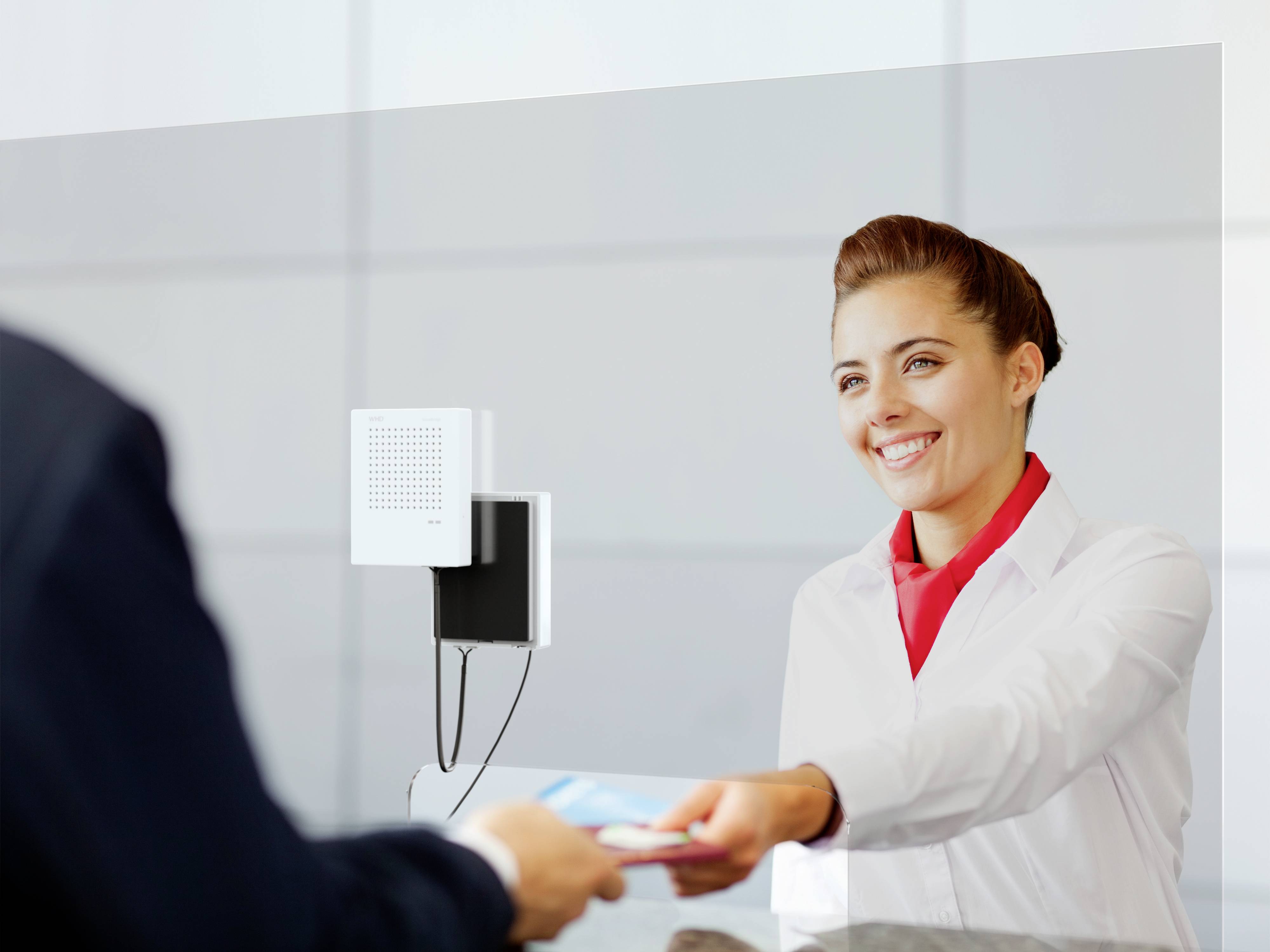 A smiling woman behind a counter is handing something back to a customer. She is wearing white service attire and has a red scarf.