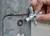 A hand is holding a cross-head spanner against a screw on a metal post. The spanner has four different head sizes.