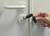 A hand holding a lock-picking tool against a white door with a door handle and lock, depicting a security risk through burglary equipment.