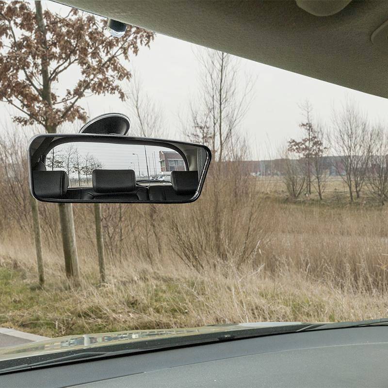 Rear-view mirror view shows a car behind on a winter country road with bare trees lining the sides.