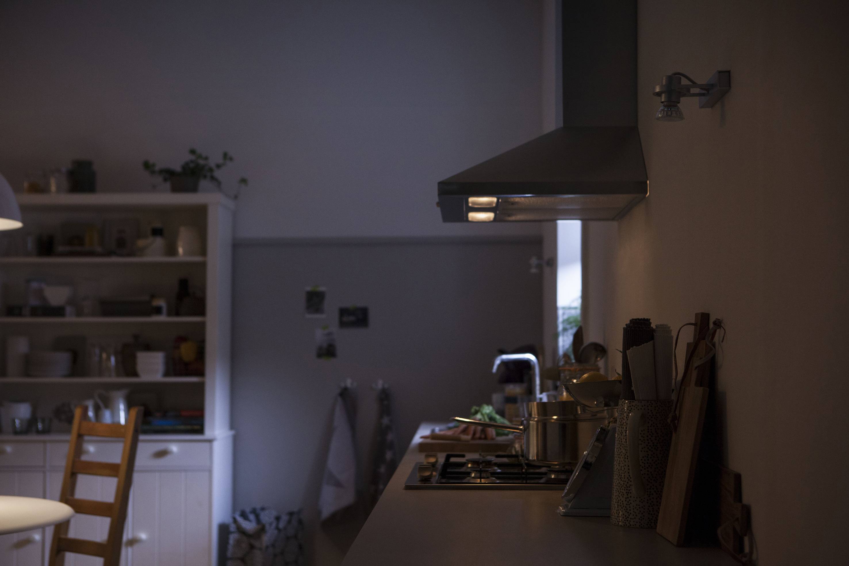 Dark kitchen with dimmed lighting, showing a cooker with a pot, next to a shelf full of crockery. Atmospheric, calm ambience.