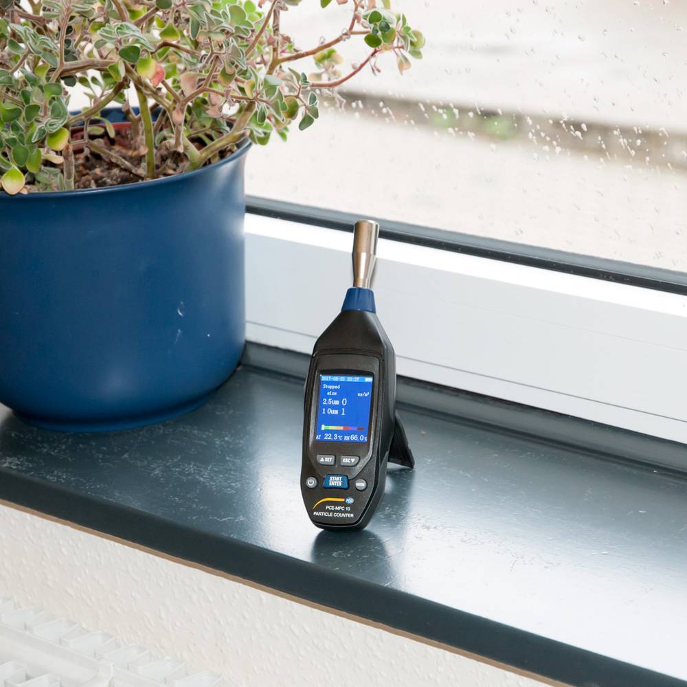 Sound level meter on windowsill shows '47.8 dB'. Next to it, a pot with green foliage. Measuring noise level near indoor plant.