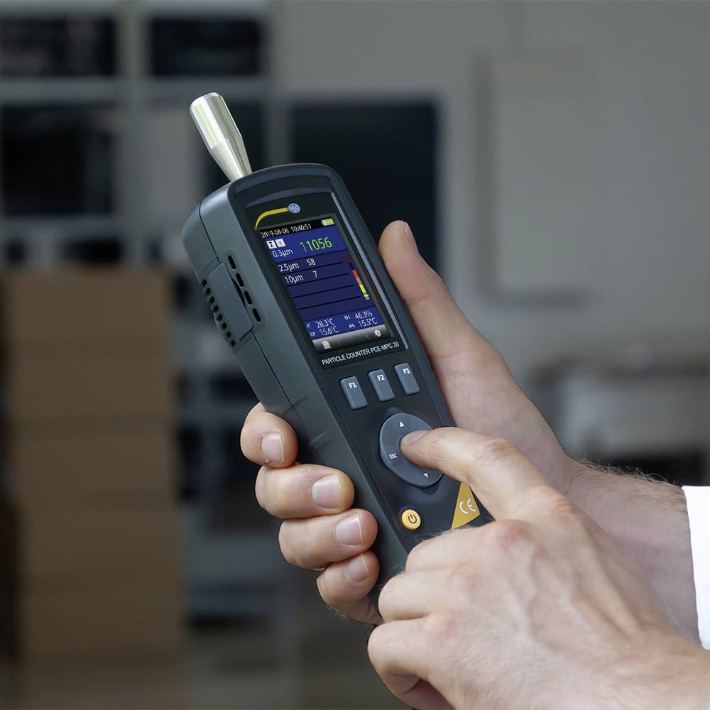 A hand is holding a portable measuring device with a display showing technical data such as temperature and humidity.