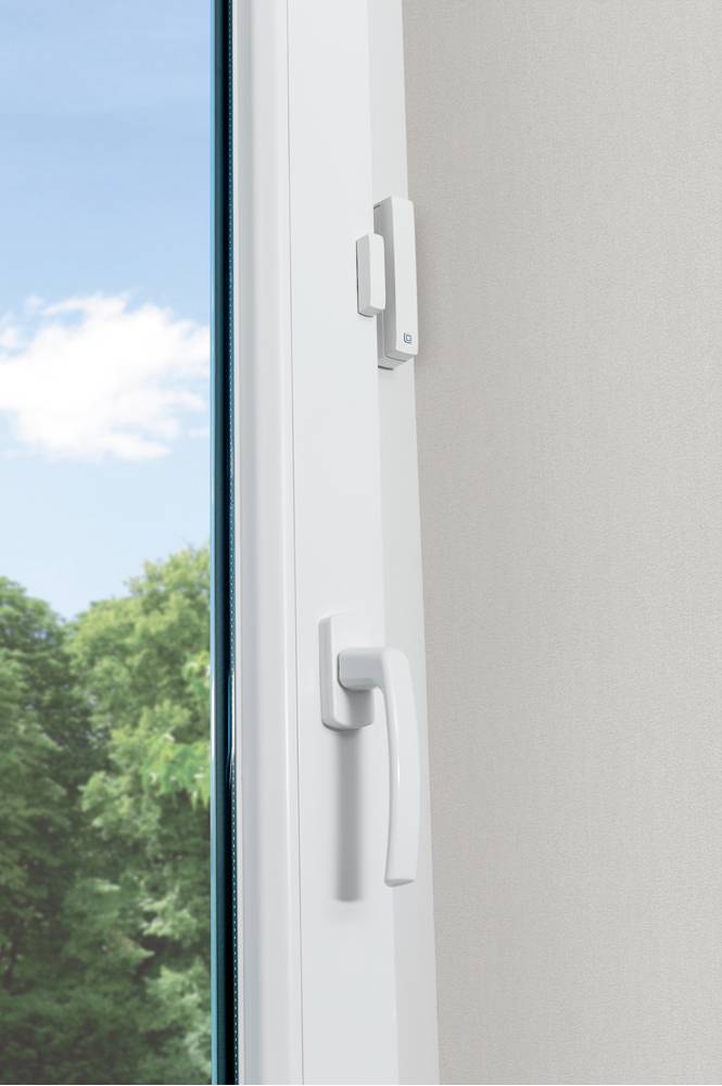 A white window handle set on an open window; trees and blue sky are visible in the background.