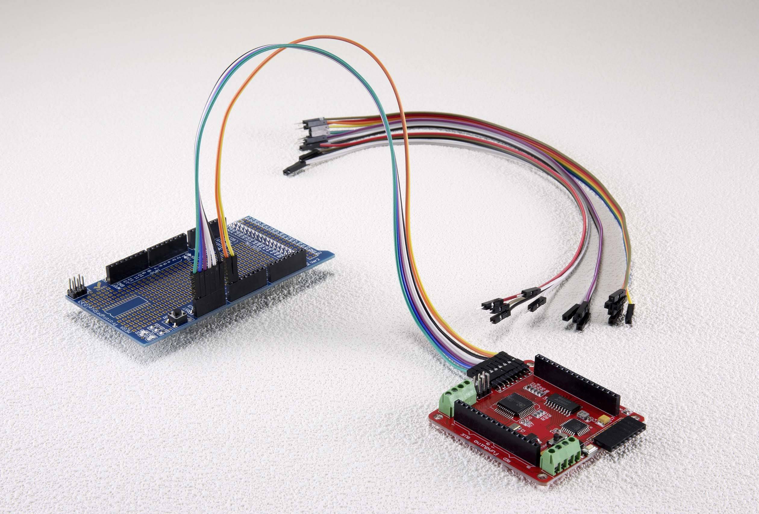 Two electronic circuit boards are connected by coloured cables. The blue circuit board is on the left, the red circuit board on the right.