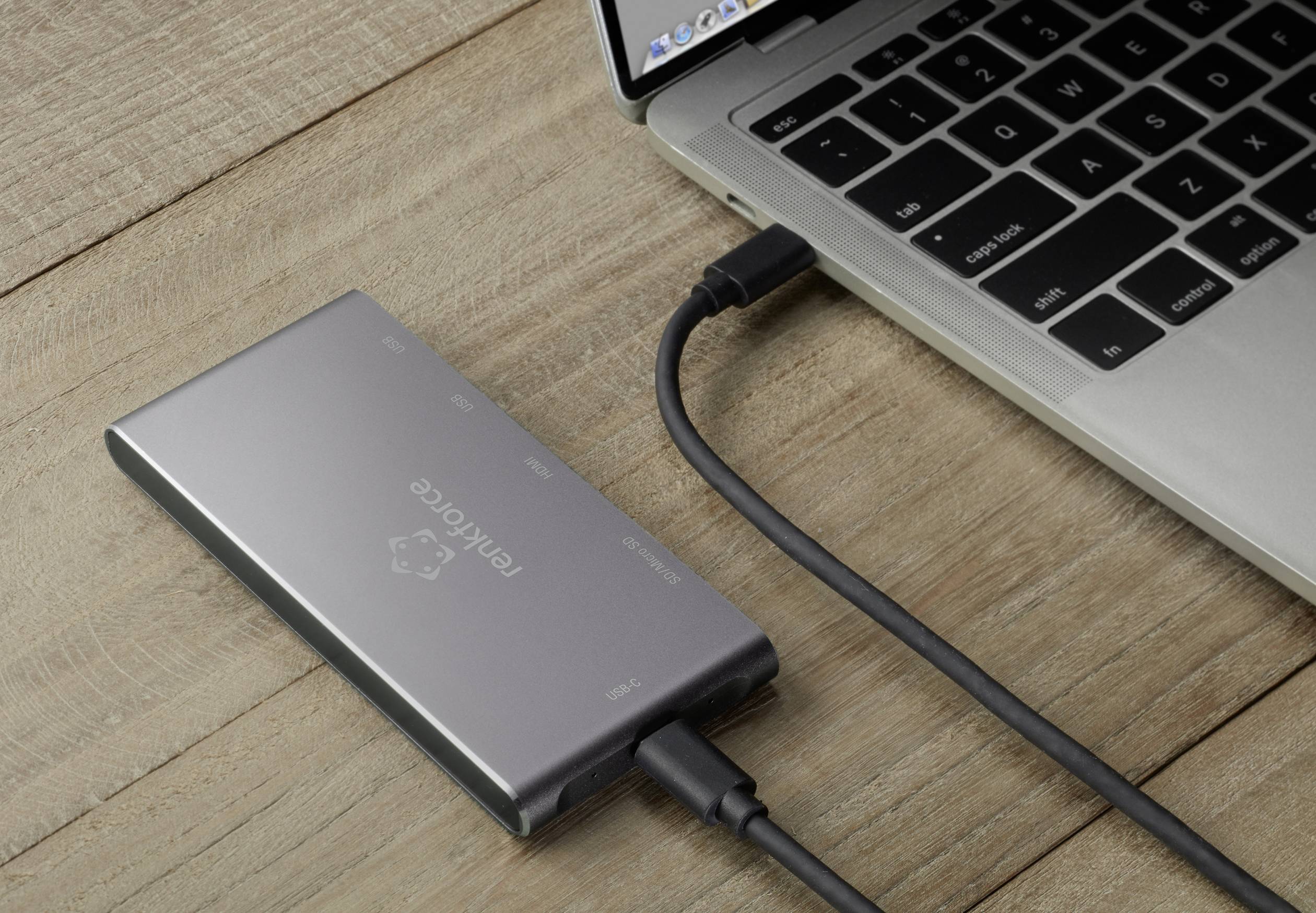 External hard drive connected to a laptop with a cable, lying on a wooden table.