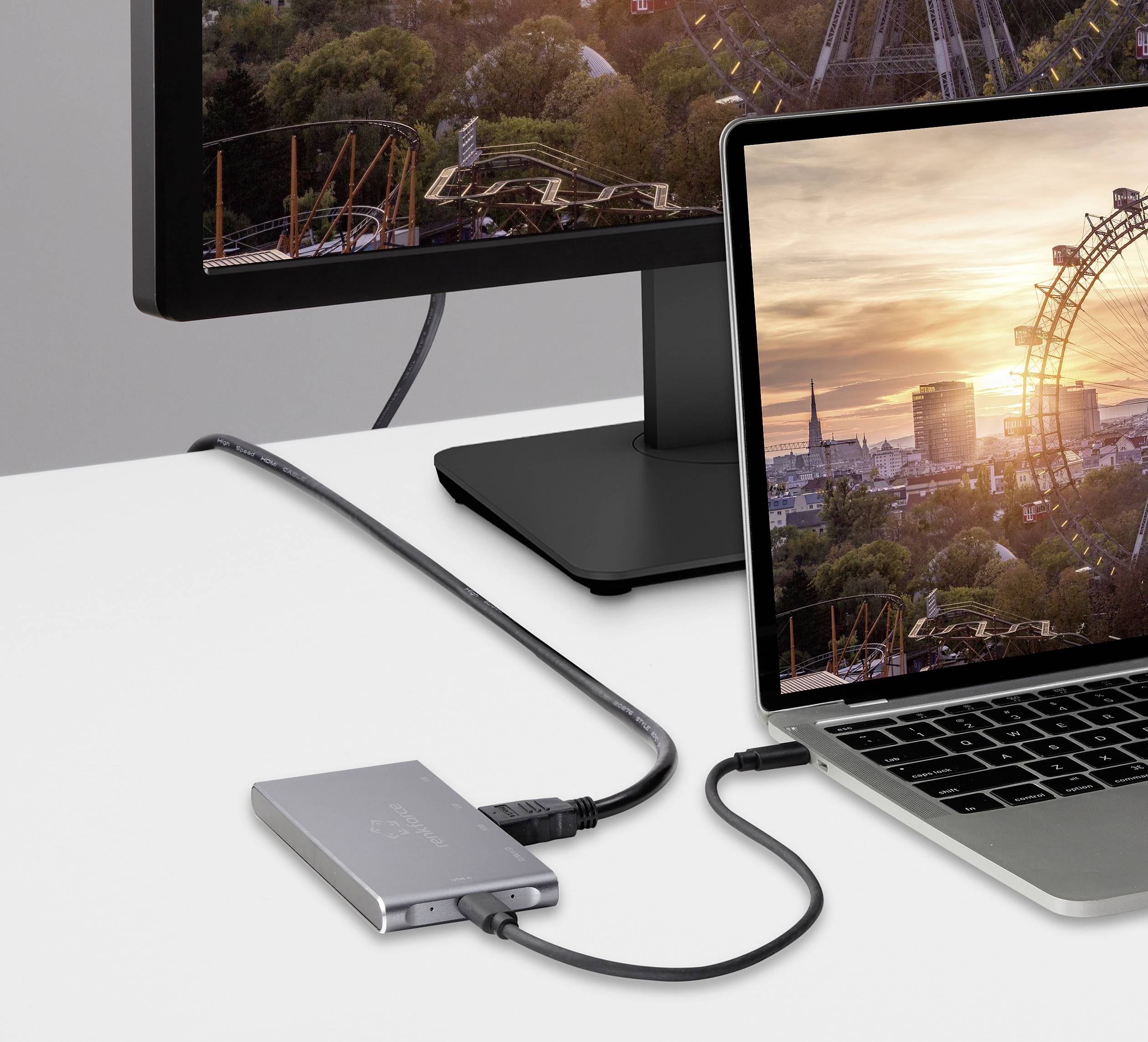 A laptop sits on a table, connected to a monitor. On both screens, a Ferris wheel and a city at sunset are visible.