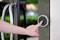 A hand is pressing a round, grey doorbell button next to a glass door with metal handles.